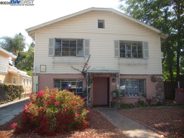 Two-story home with cream siding, a brick lower facade, and a flowering shrub by the walkway.