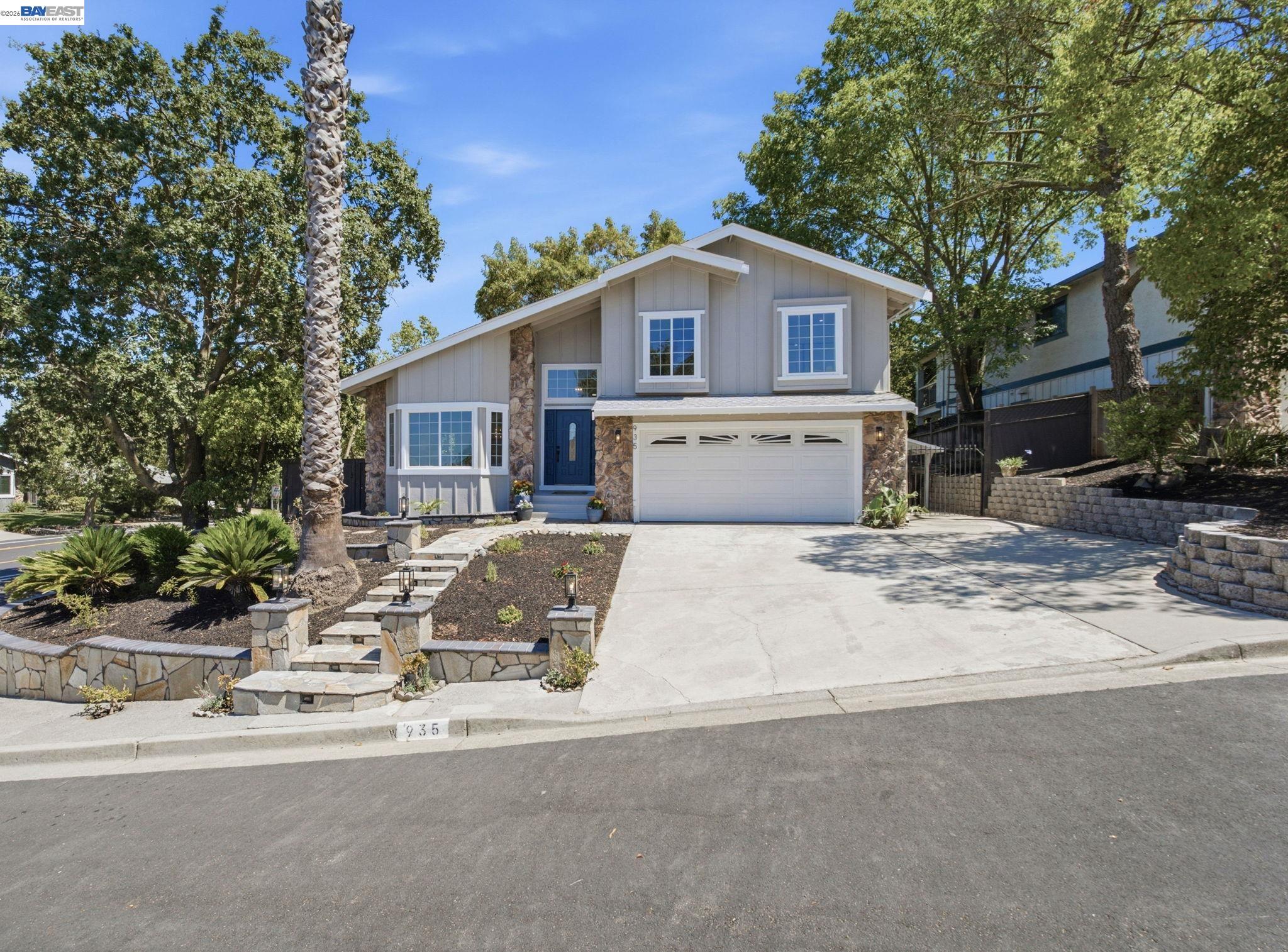 Gray two-story home with stone accents, a blue front door, double garage, and landscaped stone steps.