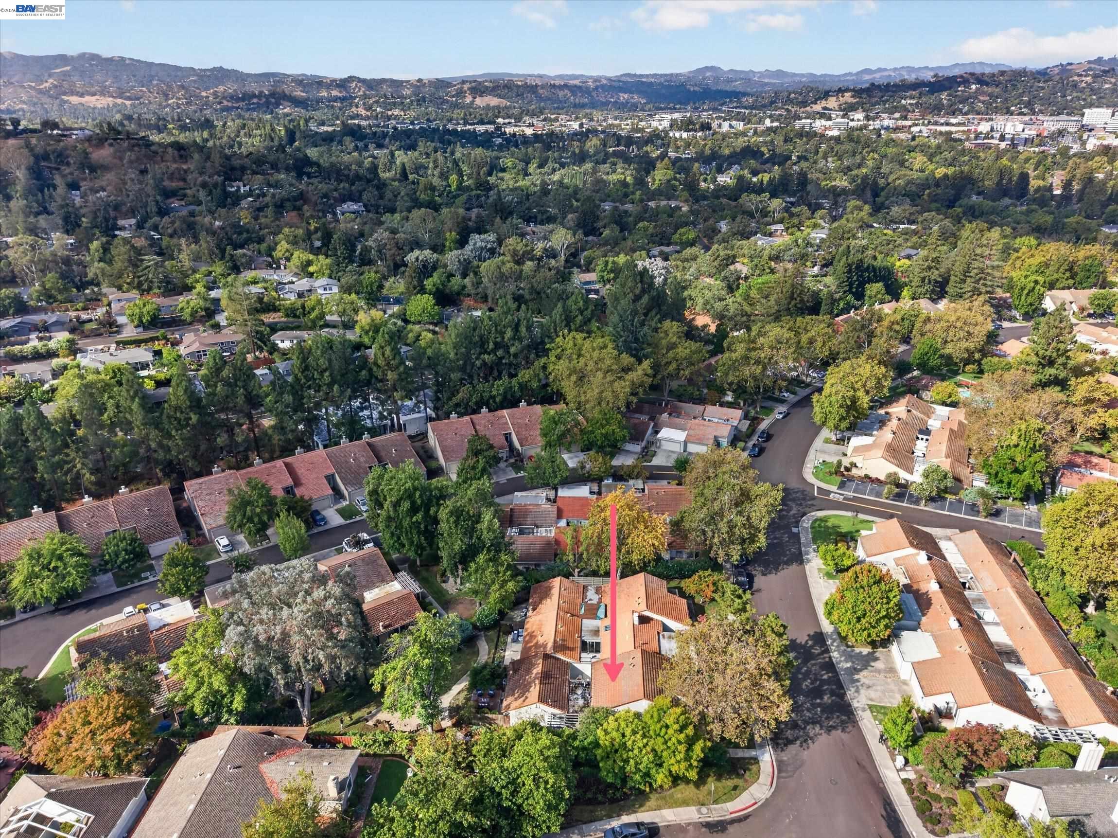 Aerial neighborhood view with a pink arrow pointing to the red-tile-roofed home.