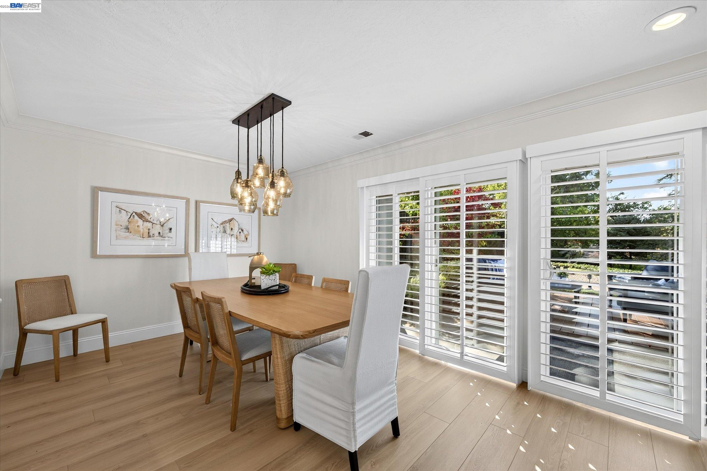 Dining room with a long wood table, pendant lights, and large plantation-shuttered windows.
