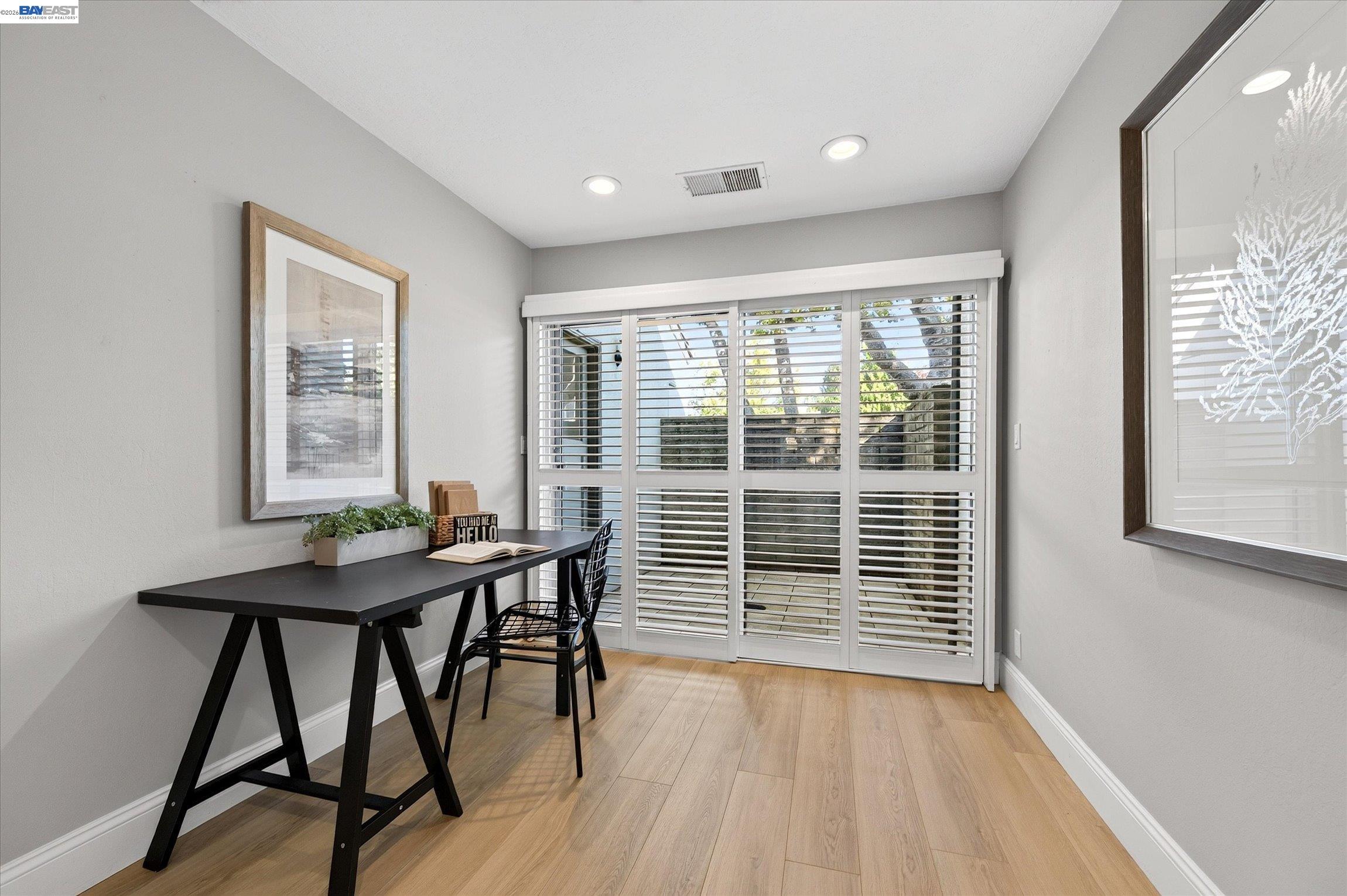 Furnished home office with a black desk and chair beside wide plantation-shuttered windows.