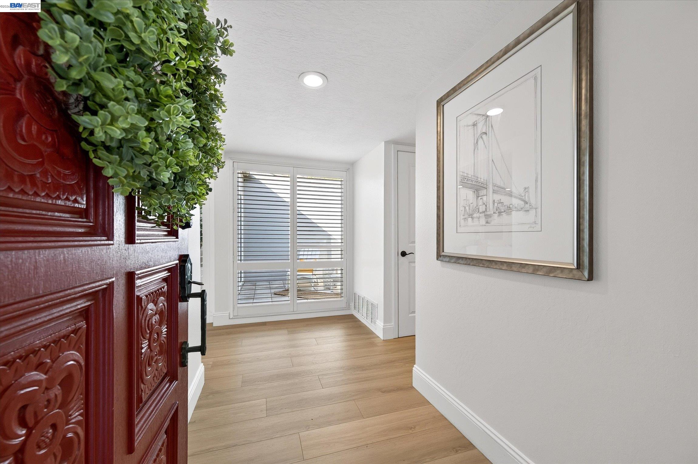 Entry foyer with an ornate red front door, wood-look flooring, and shuttered glass doors.