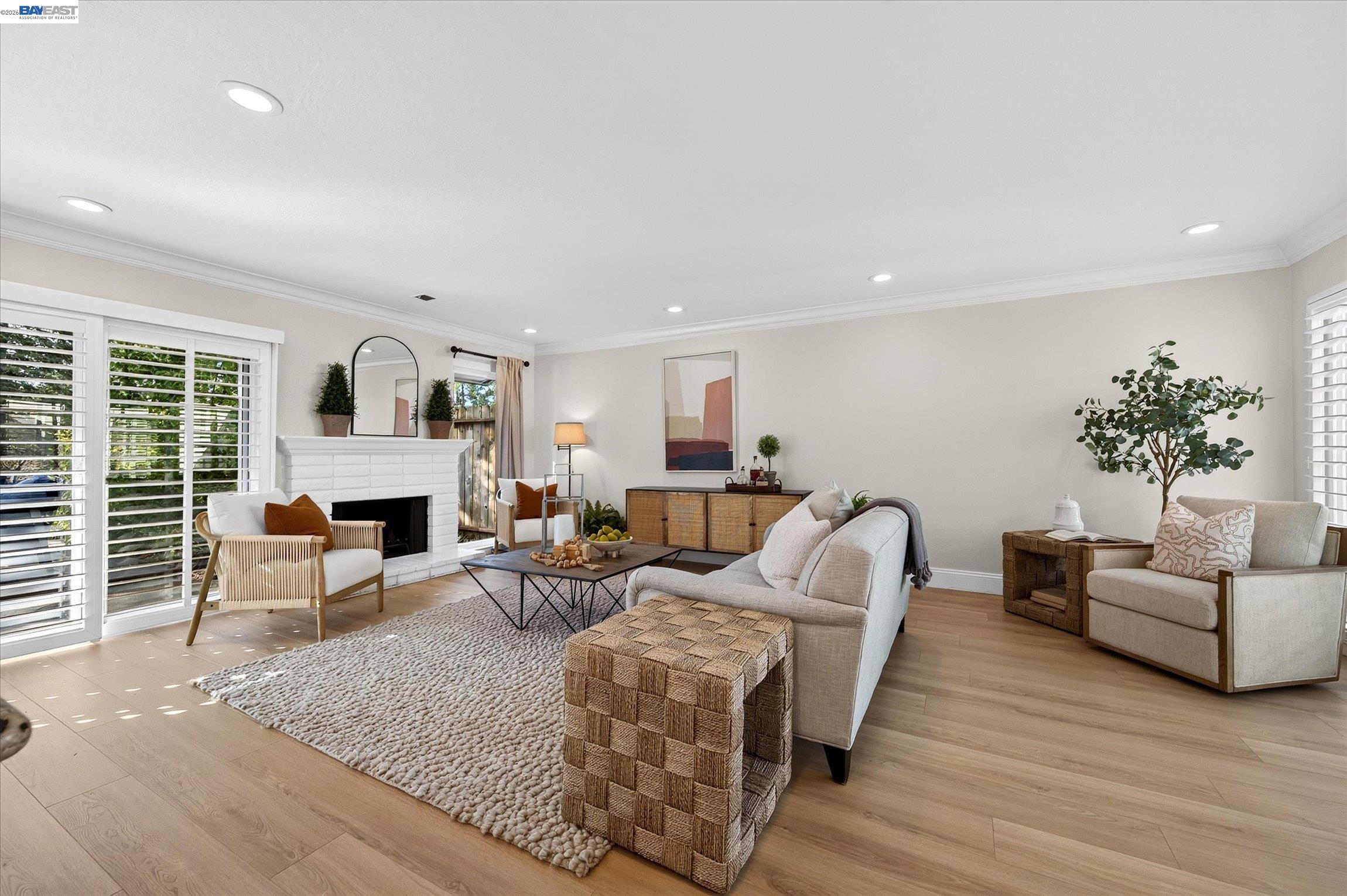 Staged living room with a white fireplace, plantation shutters, and neutral seating.