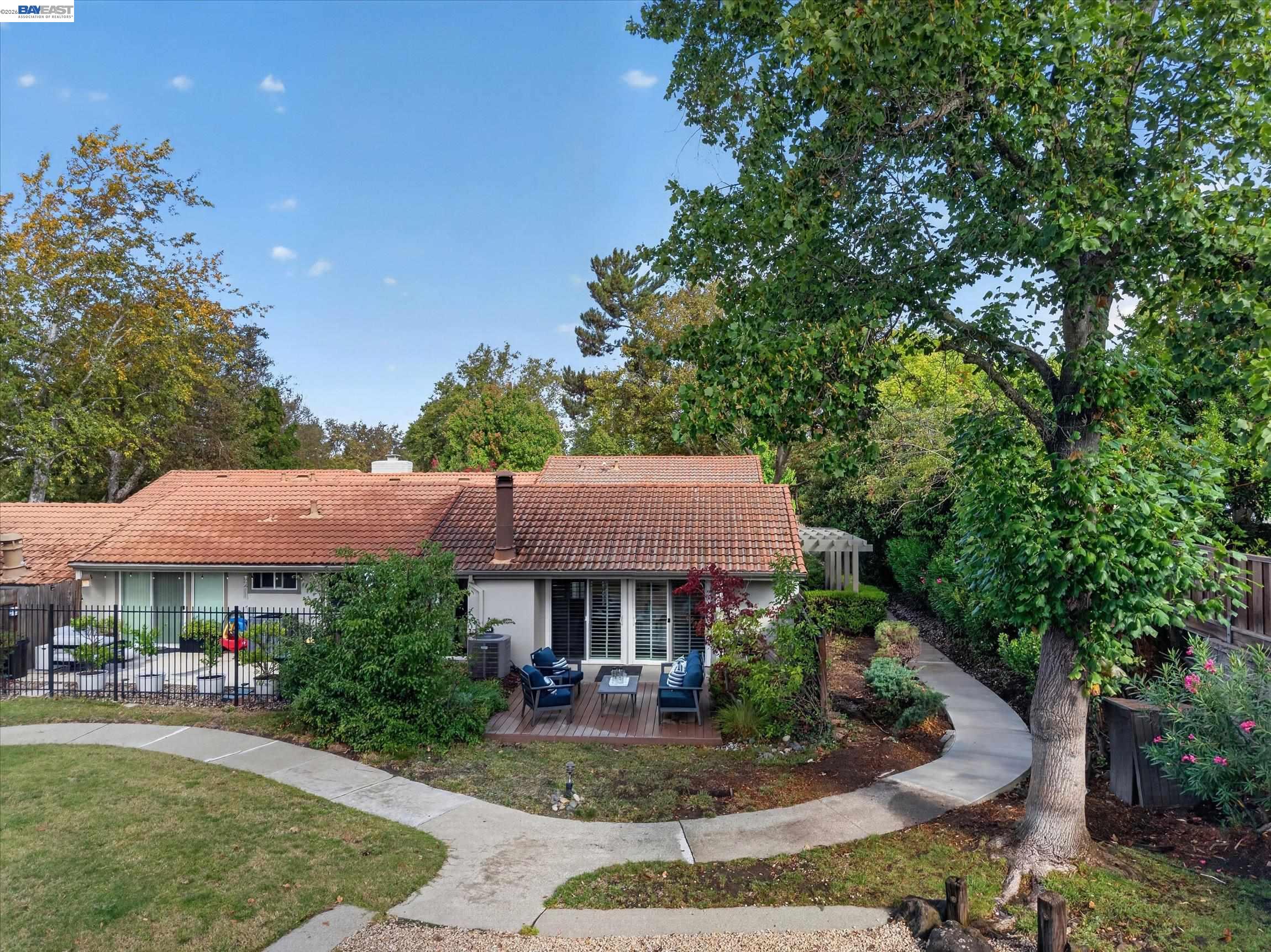 Back of a single-story home with a tiled roof, deck seating, landscaped yard, and curving walkway.