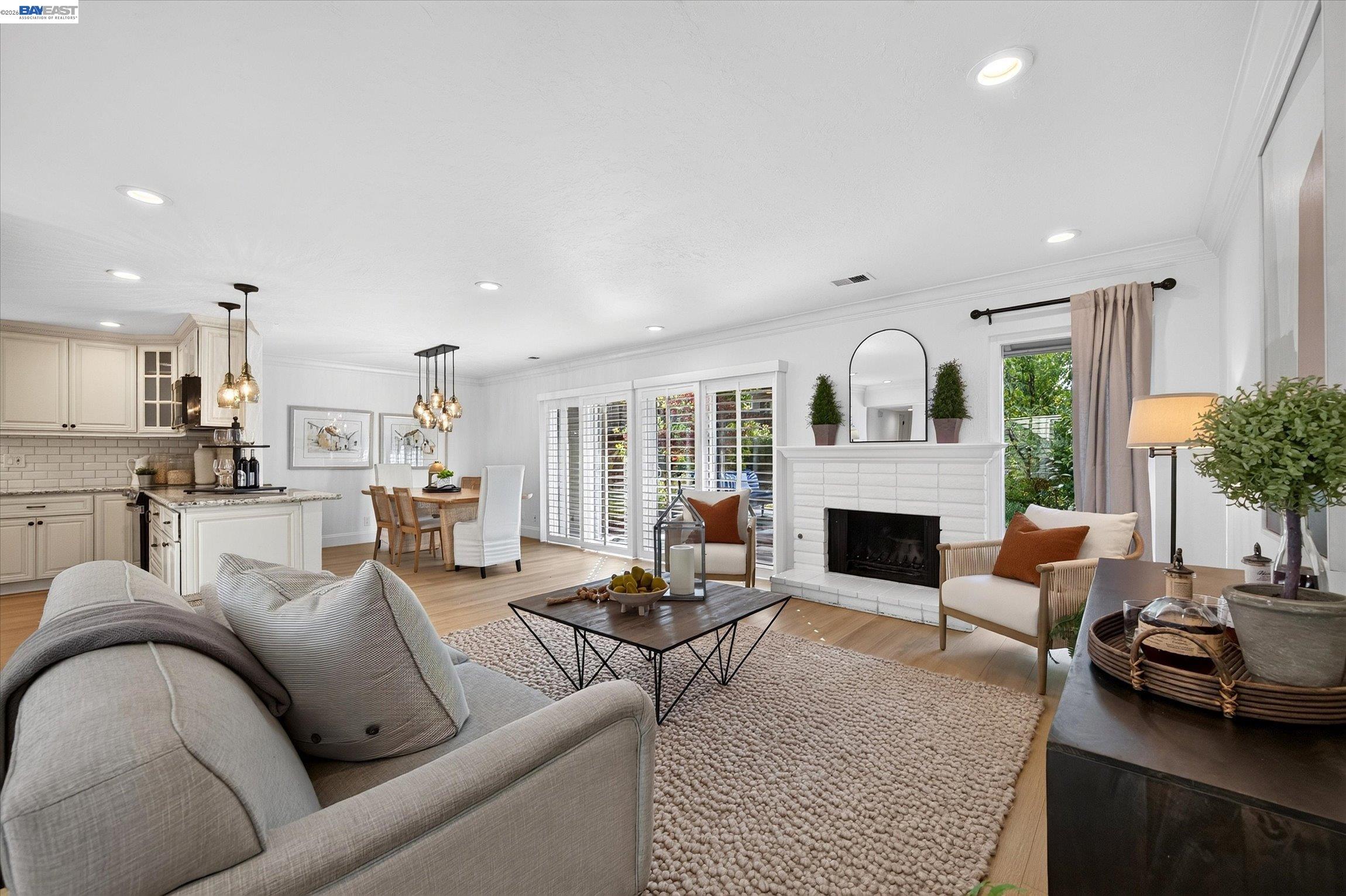 Staged living room with white brick fireplace, opening to dining area and kitchen.