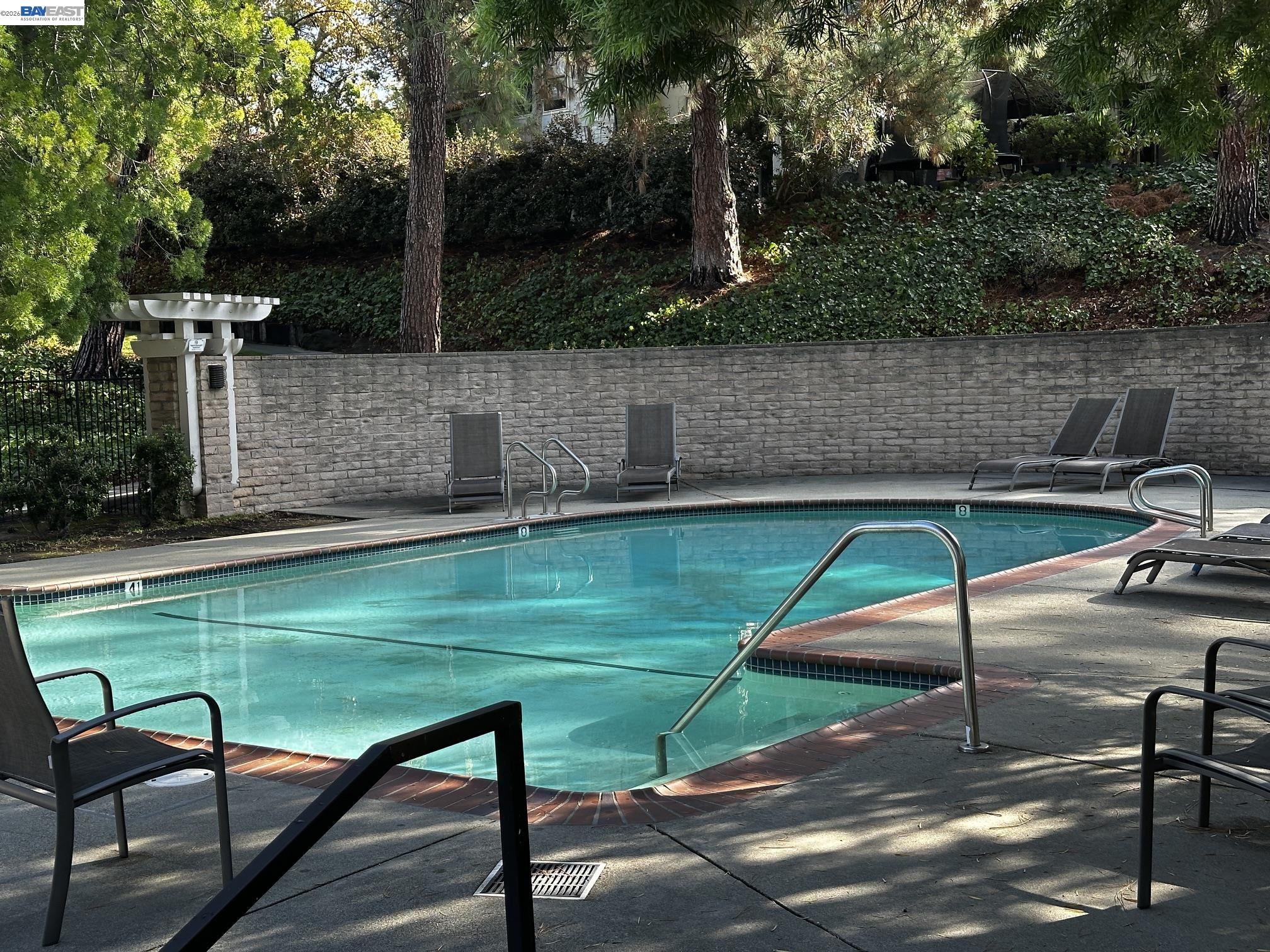 Outdoor swimming pool with curved brick edging, metal handrails, and lounge chairs beside a stone wall.
