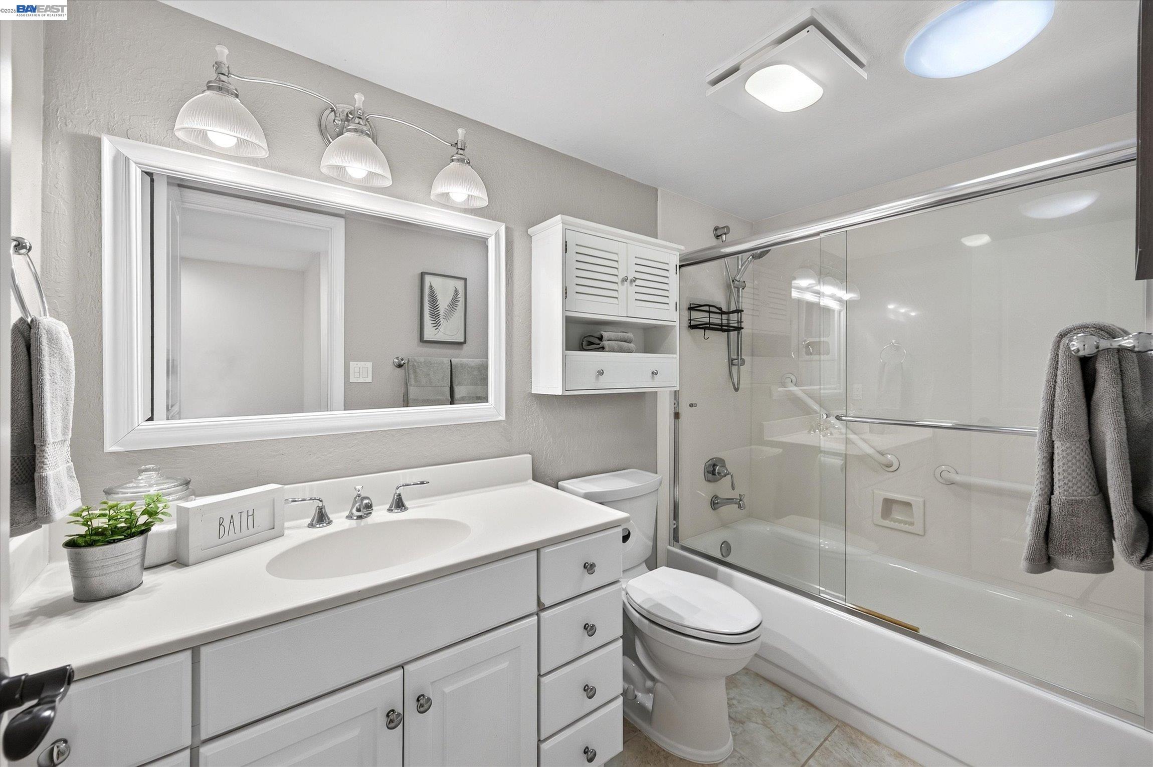 Bathroom with a white vanity and mirror beside a bathtub enclosed by clear glass.