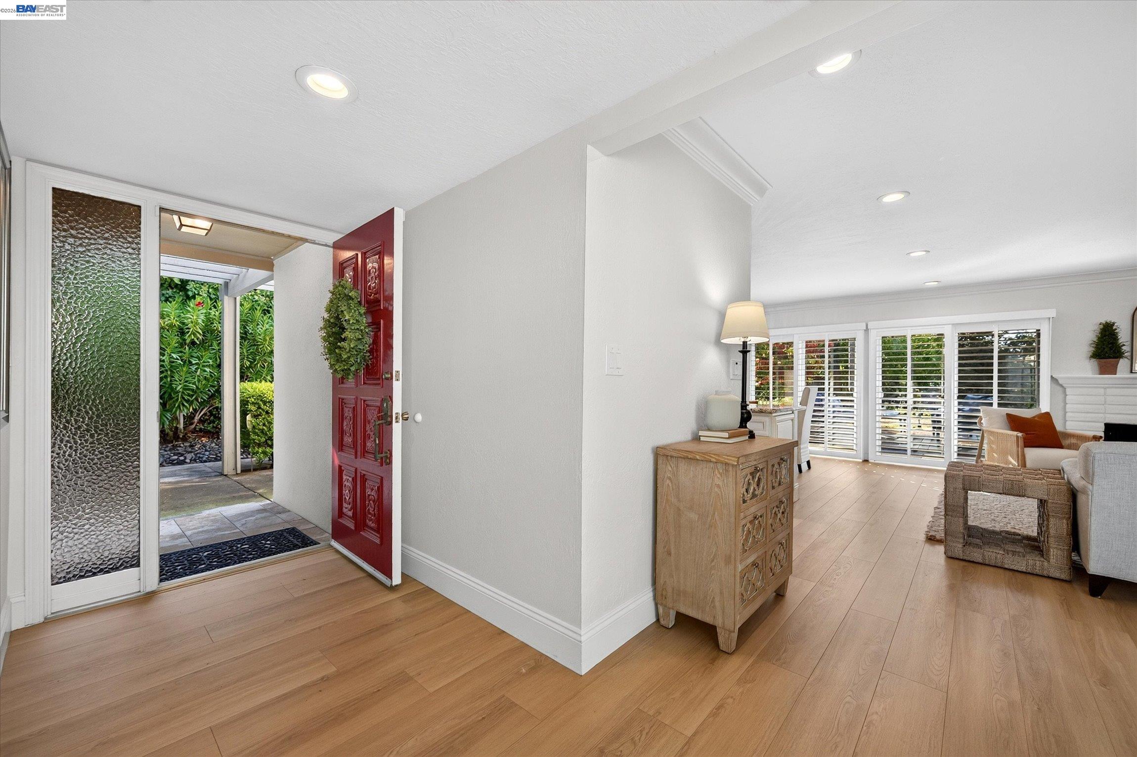 Home entry with an open red door leading to a bright living room with plantation shutters.