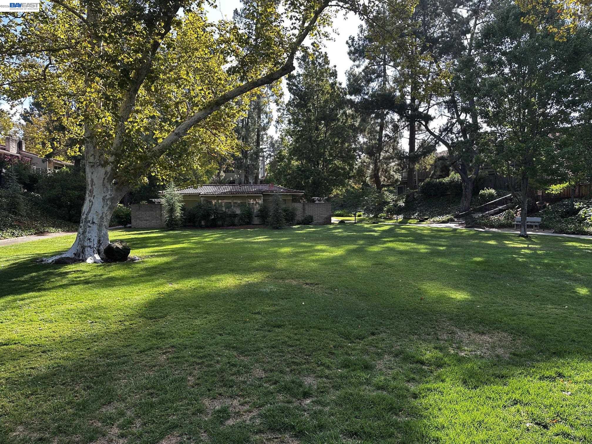 Spacious lawn beneath mature trees, with a low building and garden stairs in the background.