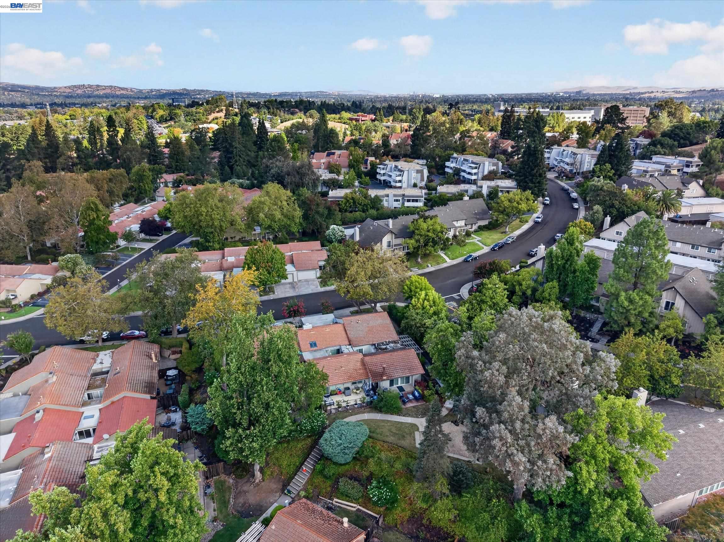 Aerial view of a leafy residential neighborhood with curving streets and distant hills.