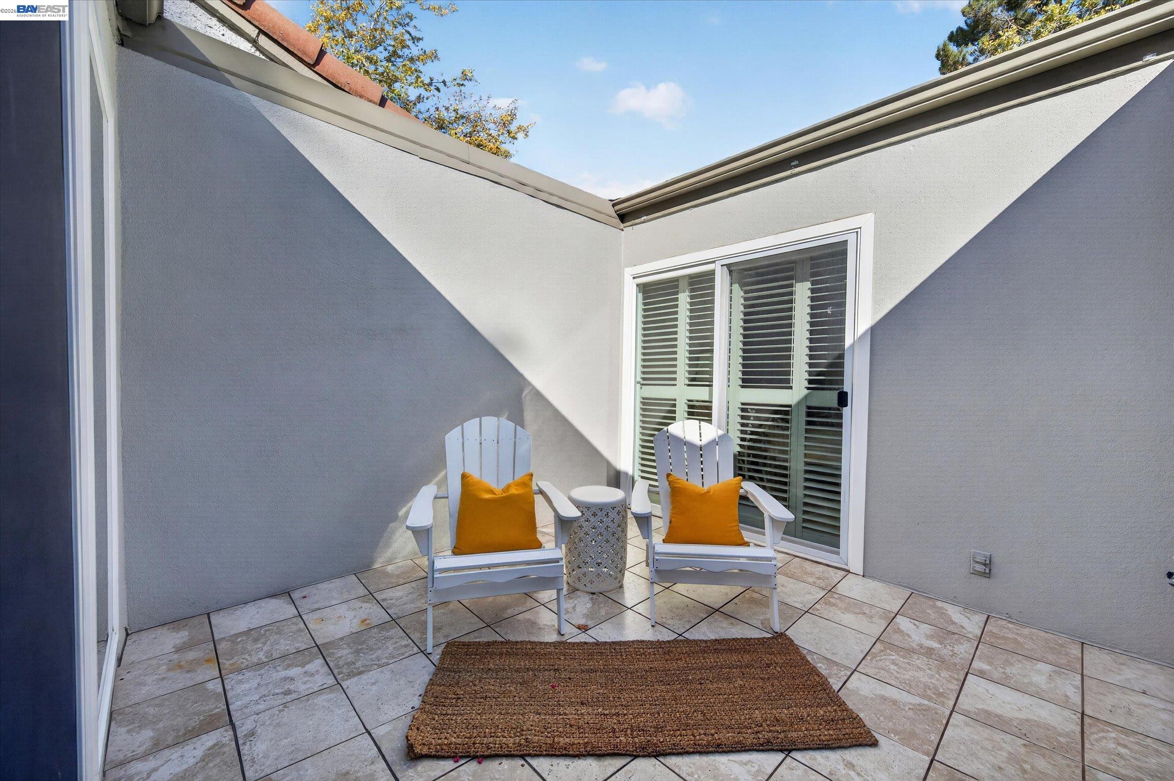 Tiled patio with two white Adirondack chairs and orange cushions beside shuttered sliding doors.