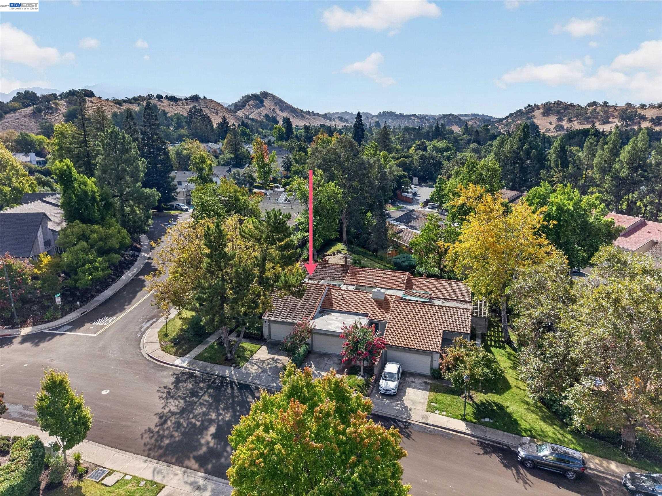 Aerial view of a red-tile-roof home marked by a pink arrow, surrounded by trees and rolling hills.