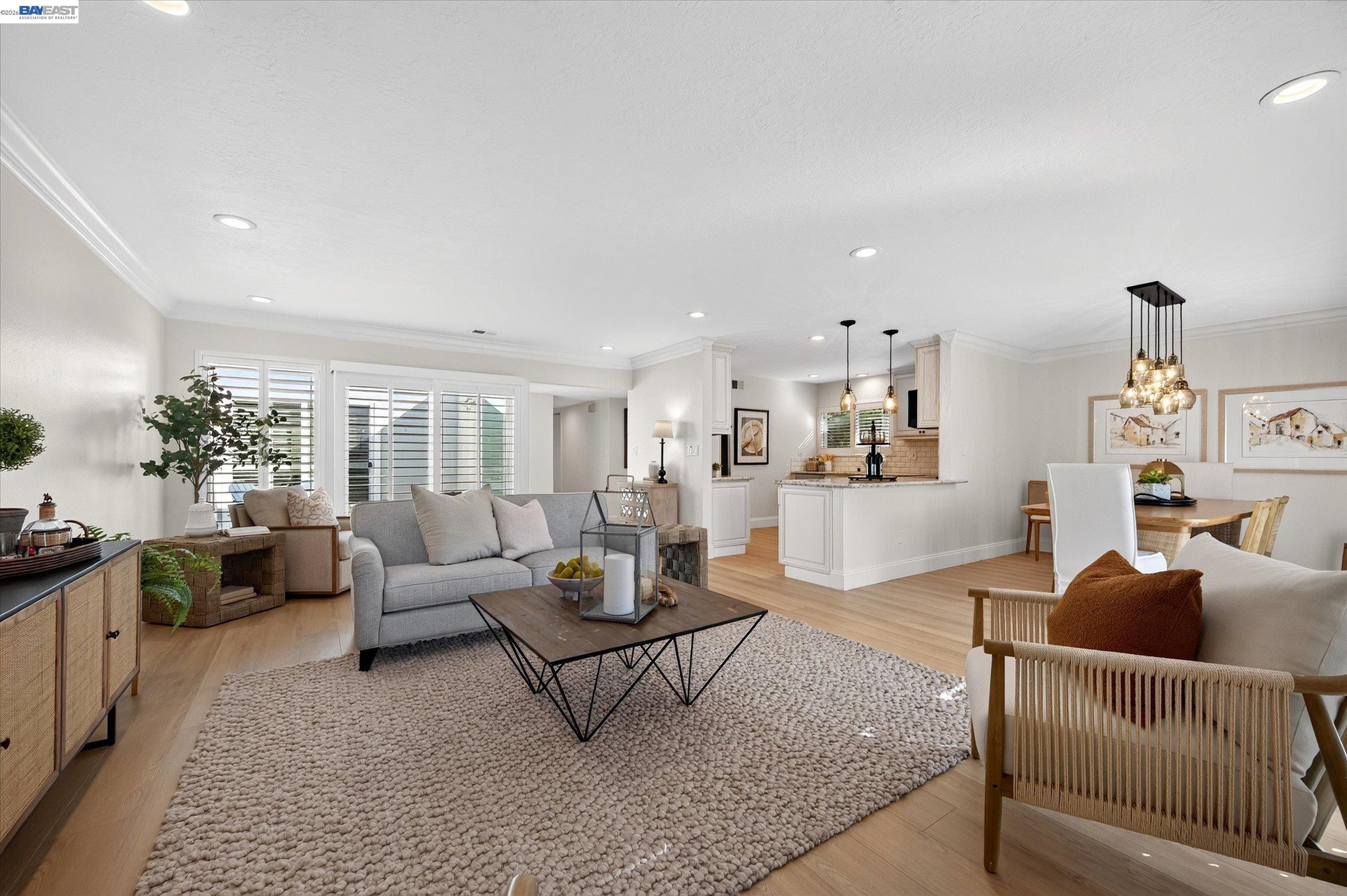 Open-plan living room with gray sofa, large textured rug, and adjoining white kitchen and dining area.