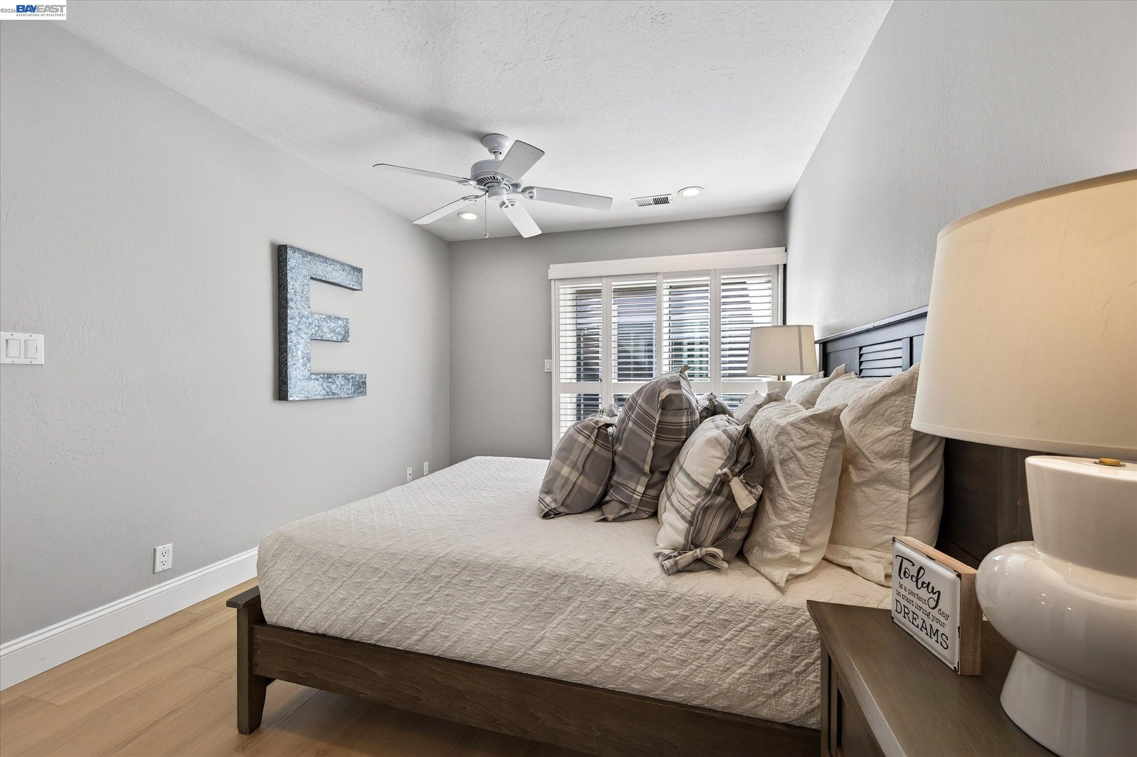 Bedroom with a dark wood bed, layered neutral pillows, shuttered windows, and a ceiling fan.