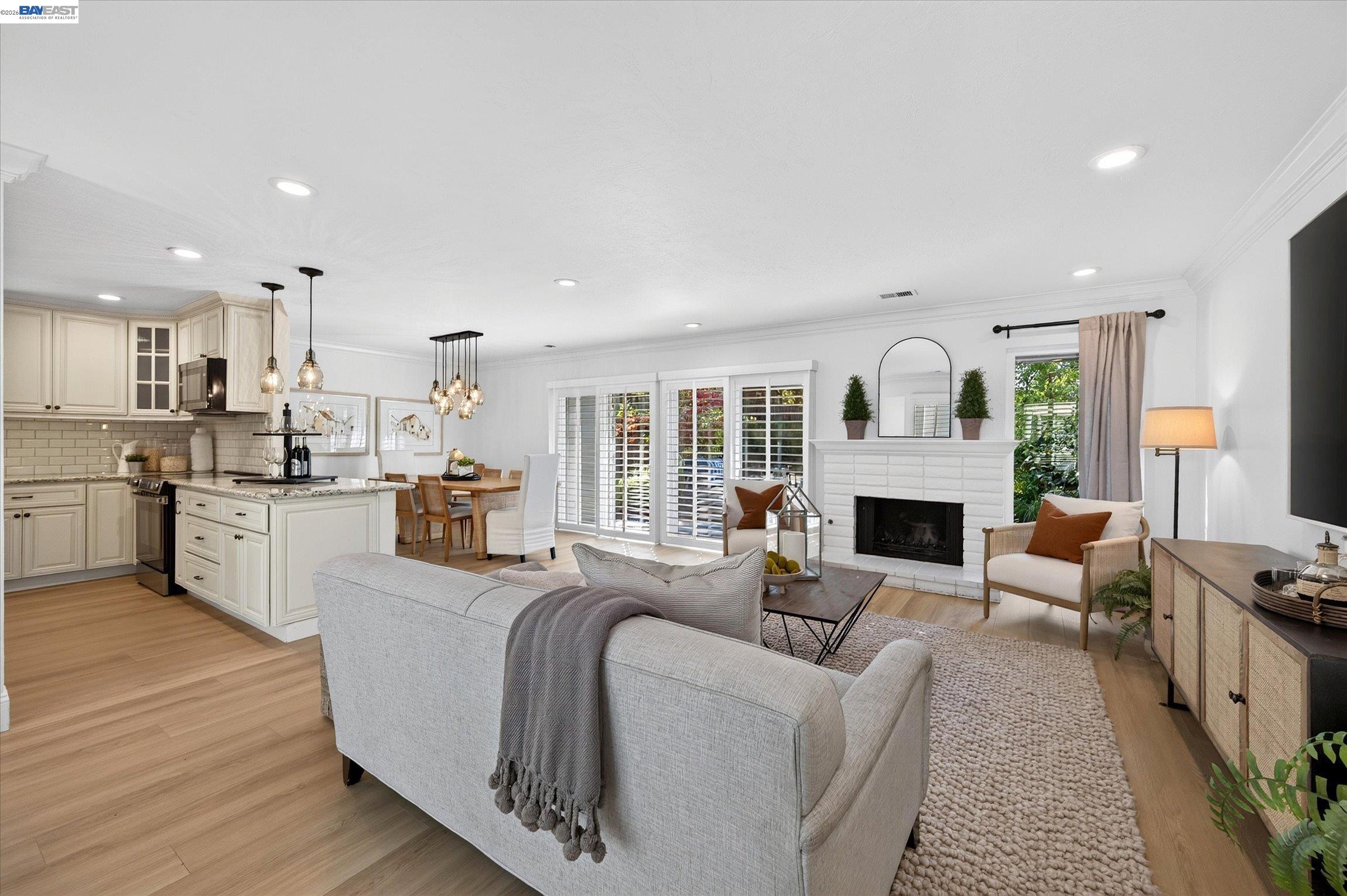 Open-plan living room and kitchen with cream cabinetry, a white fireplace, and large shuttered windows.