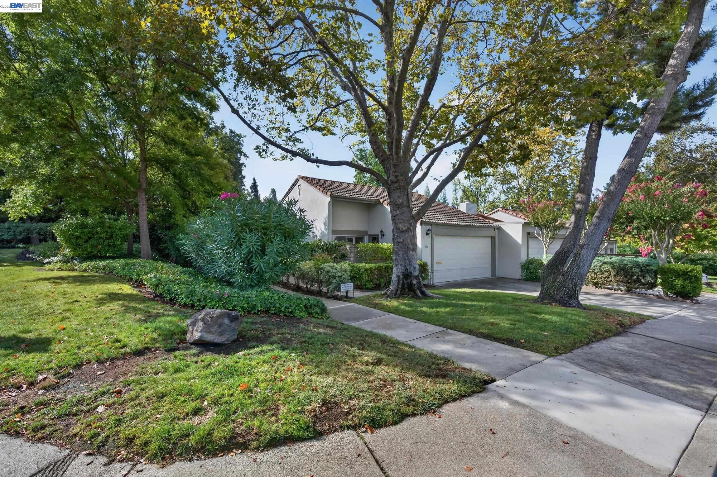 Single-story home with tiled roof and attached garage, framed by mature trees and landscaped gardens.