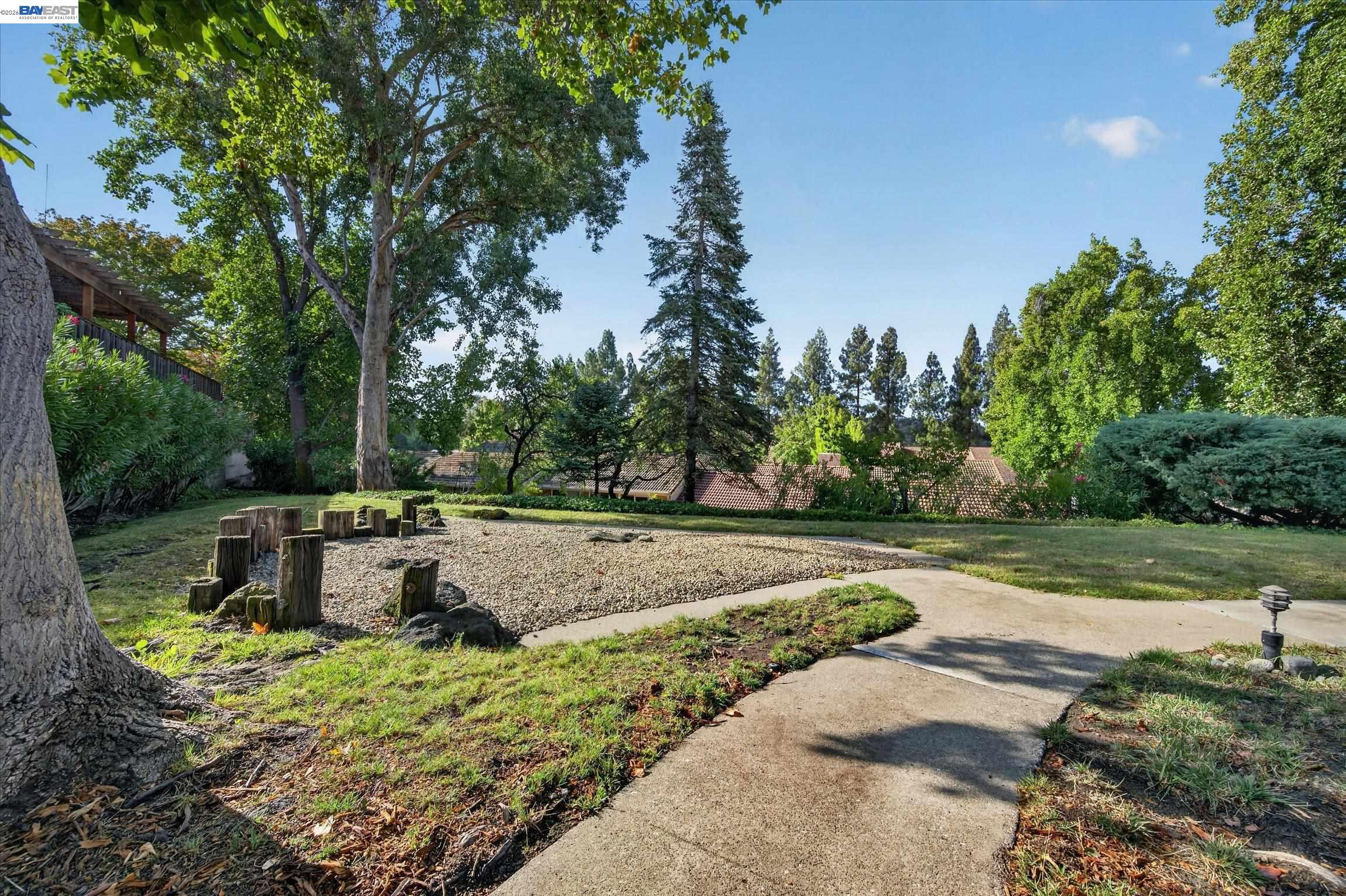 Landscaped yard with a curving walkway and gravel seating area edged by tree stumps.