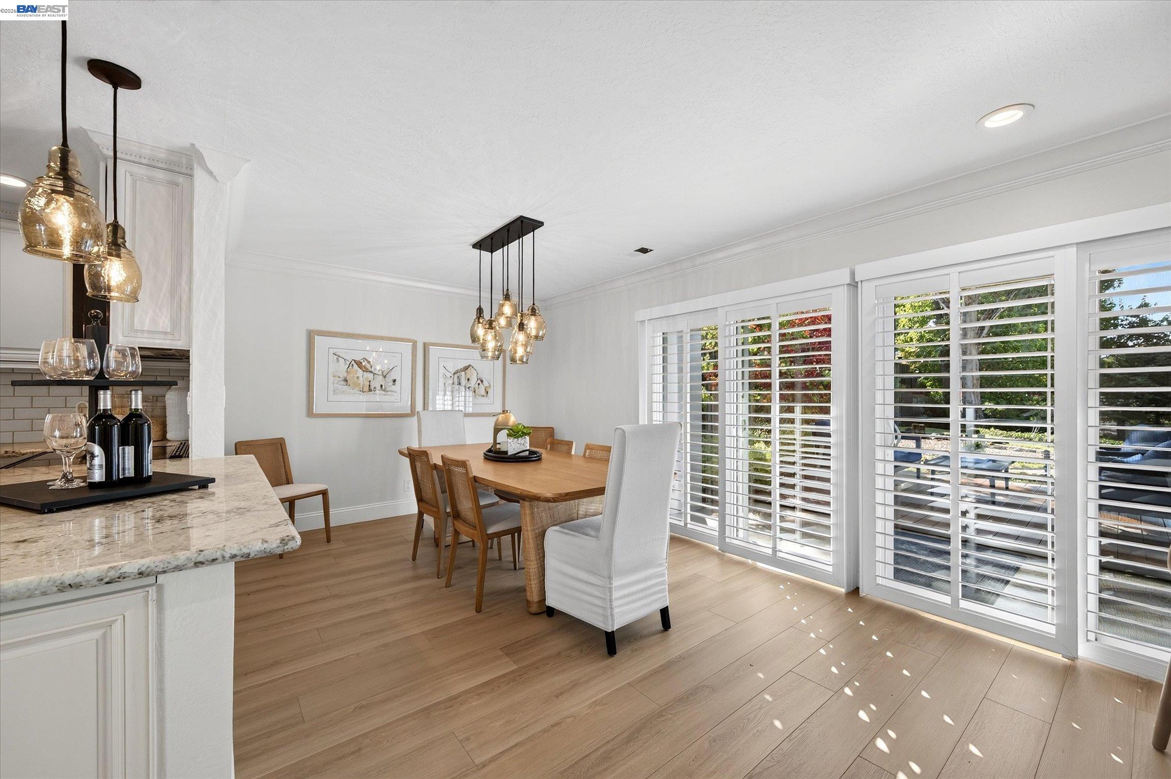Dining area with a wood table, pendant lights, and wide plantation-shuttered windows.