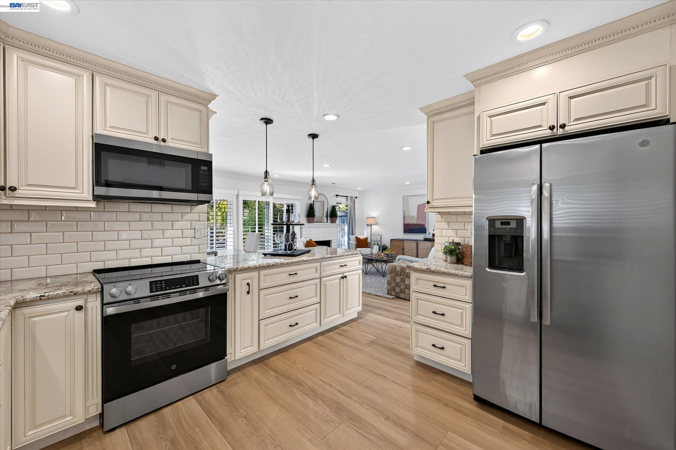 Bright kitchen with cream cabinets, stainless steel appliances, granite counters, and an island opening to the living area.