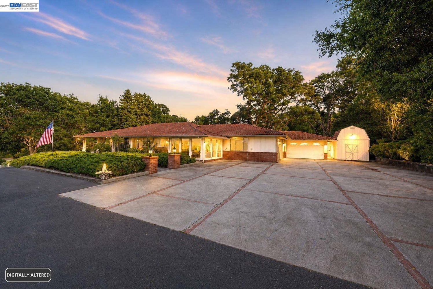Single-story home with a red tile roof, broad paved driveway, attached garage, and detached shed.