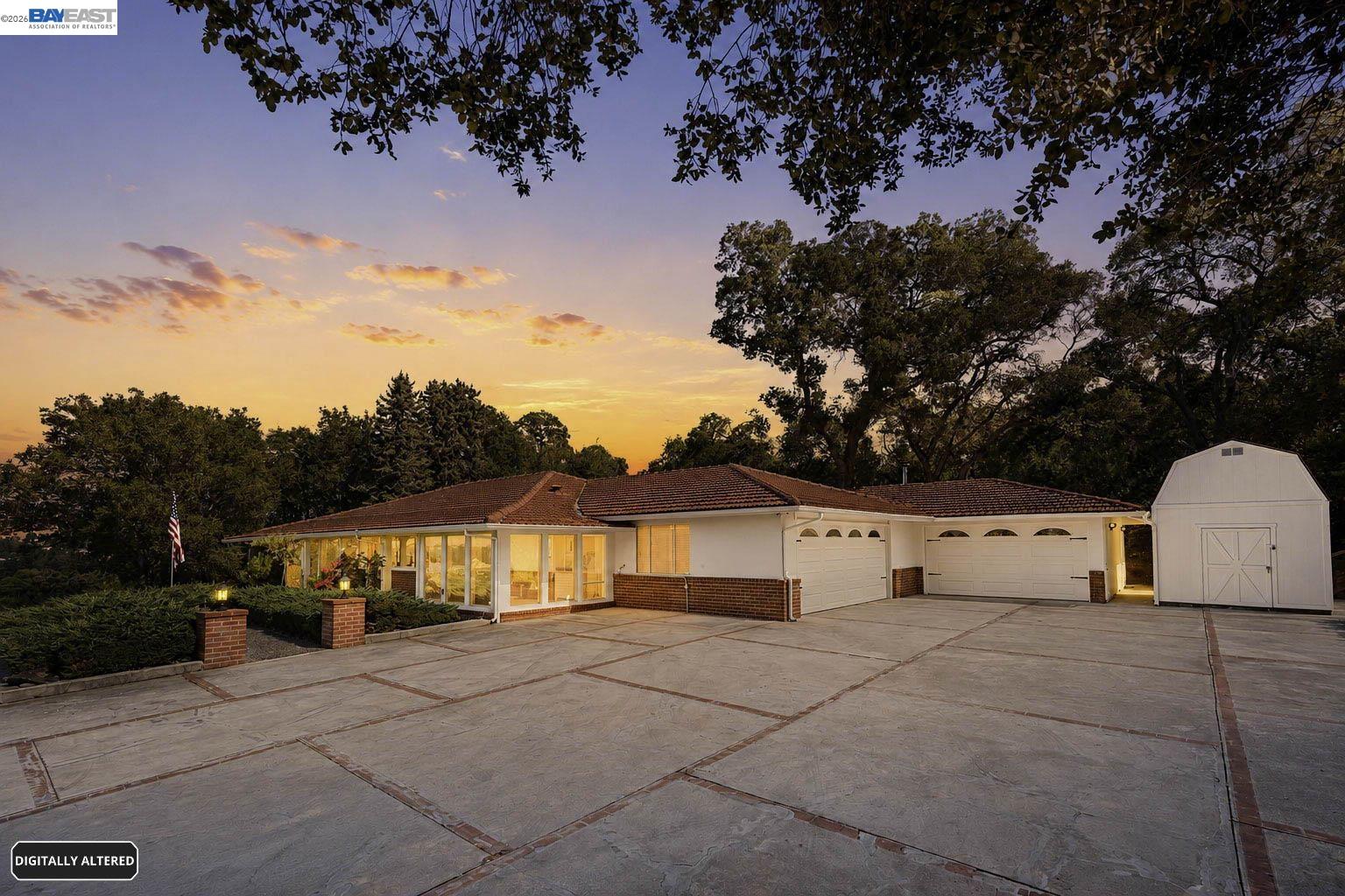 Single-story home with attached garages and a broad paved driveway beneath a sunset sky.