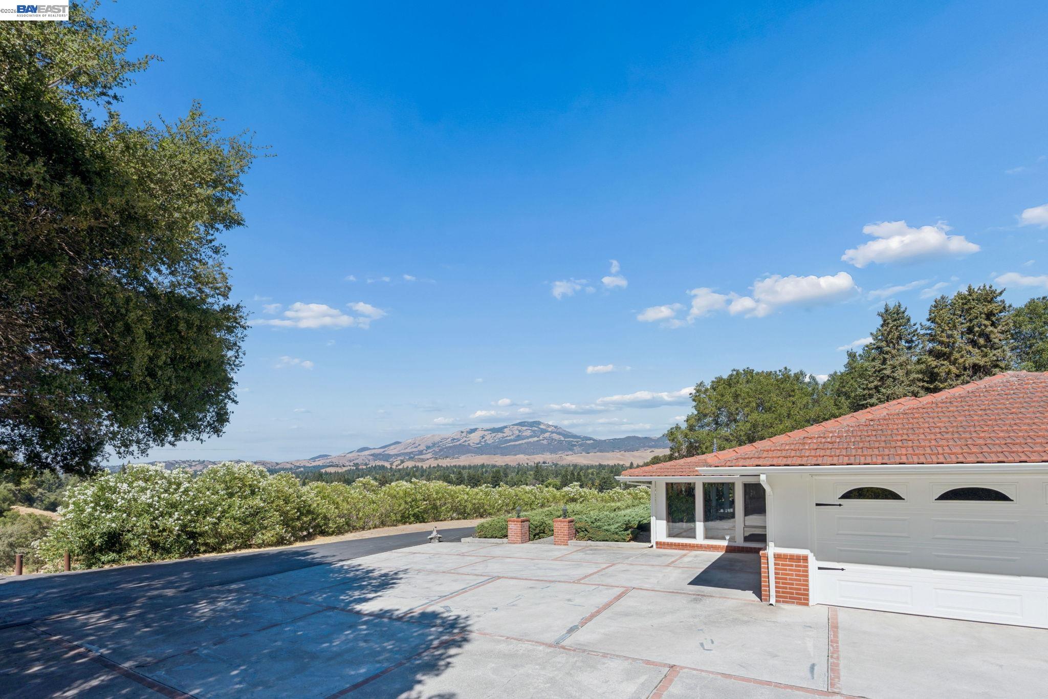 Home with a broad paved driveway, white garage, and distant rolling hills.