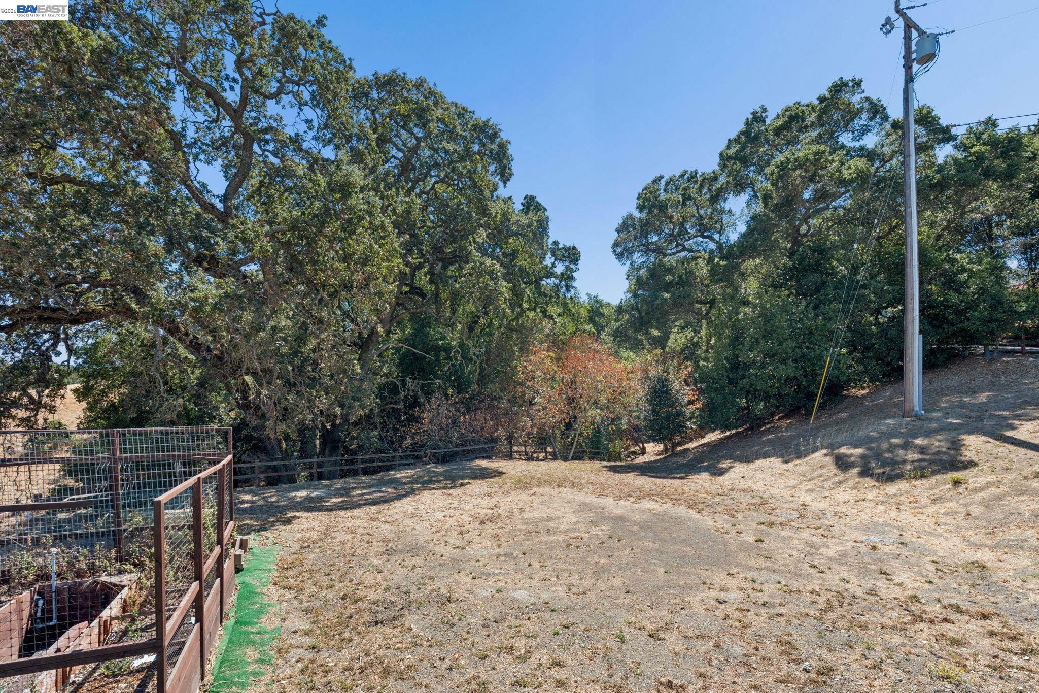 Dry sloping property lot with mature oaks, a fenced area, and a utility pole.