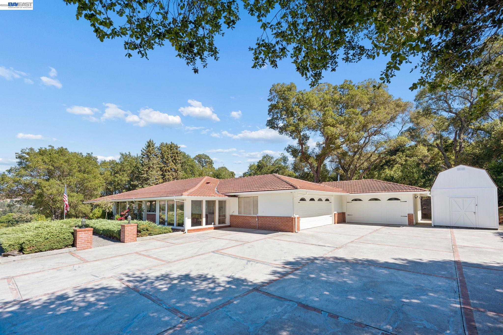 Single-story home with a broad paved driveway, two garage doors, and a detached white shed.