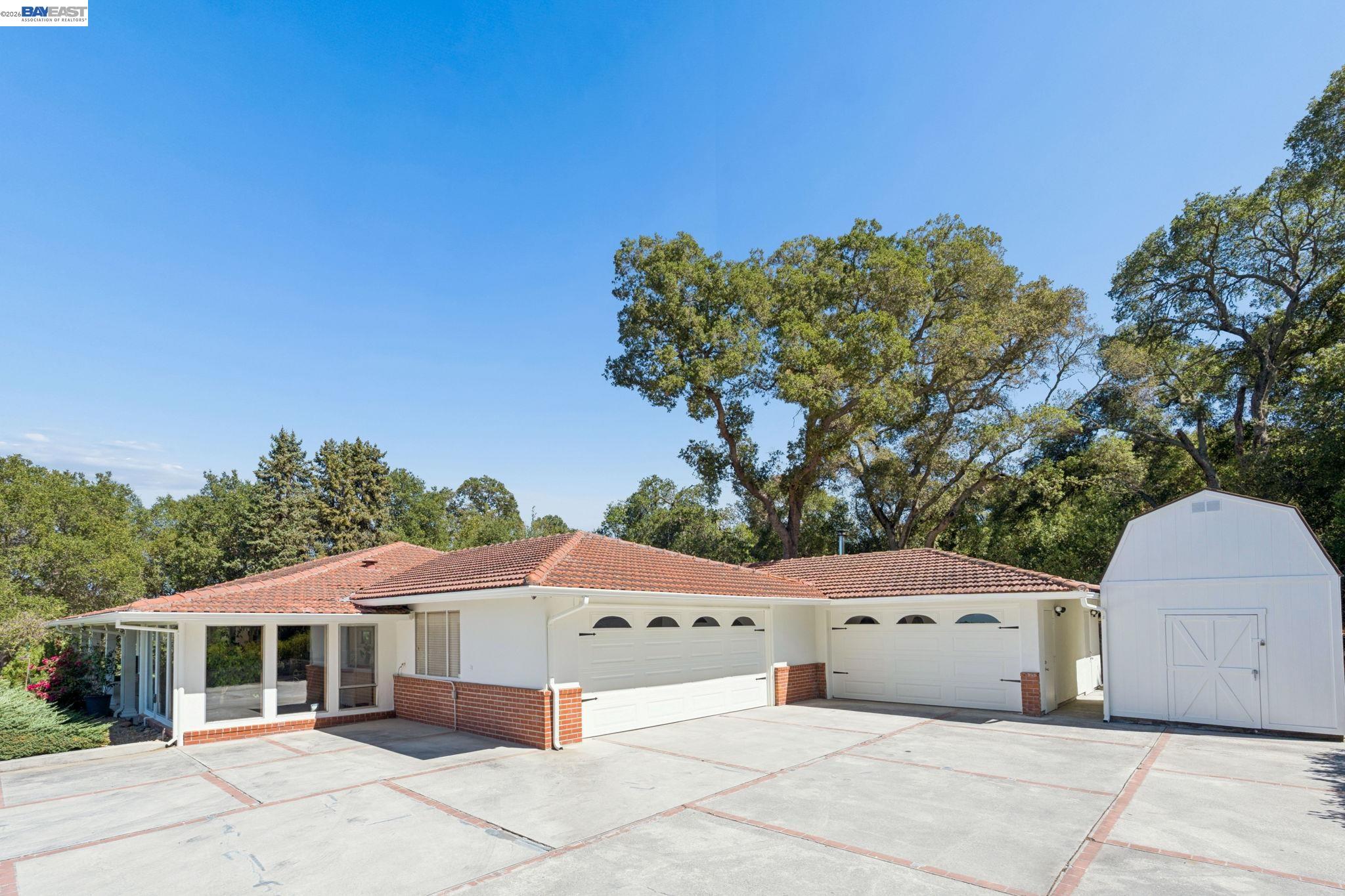 Single-story home with two garages, a wide driveway, and a detached white shed.