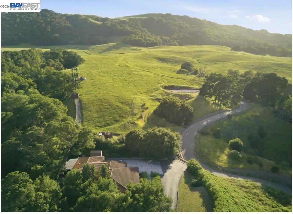 Aerial view of a rural property with rolling green hills, wooded ridges, and a winding driveway.