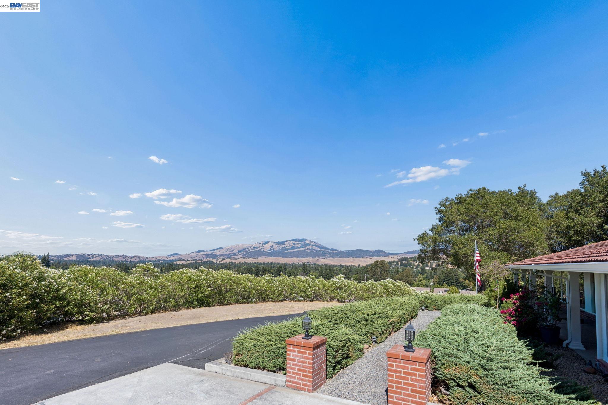 Landscaped home entrance with brick pillars, a covered porch, and distant mountain views.