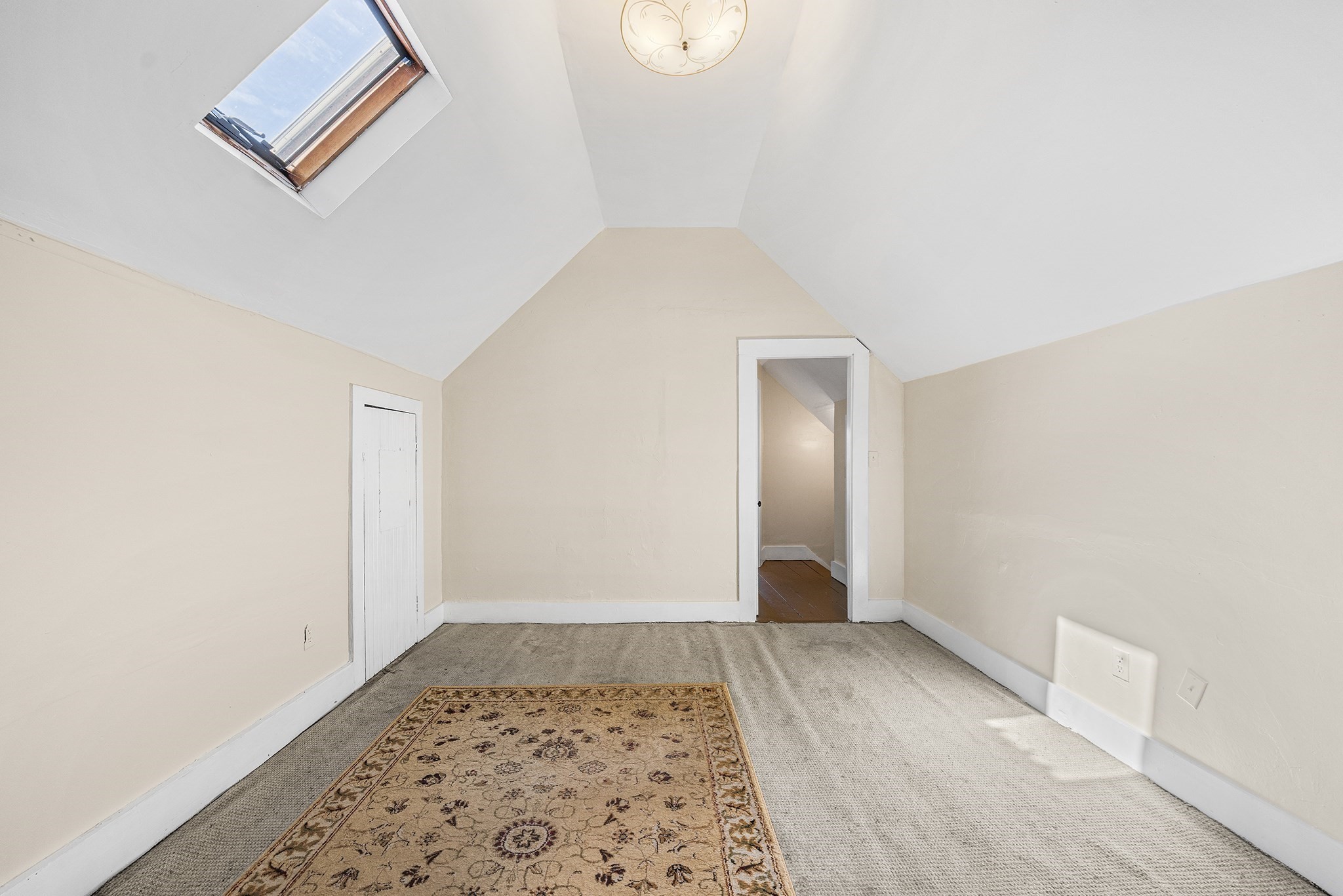 Attic room with a sloped ceiling, skylight, and patterned rug.