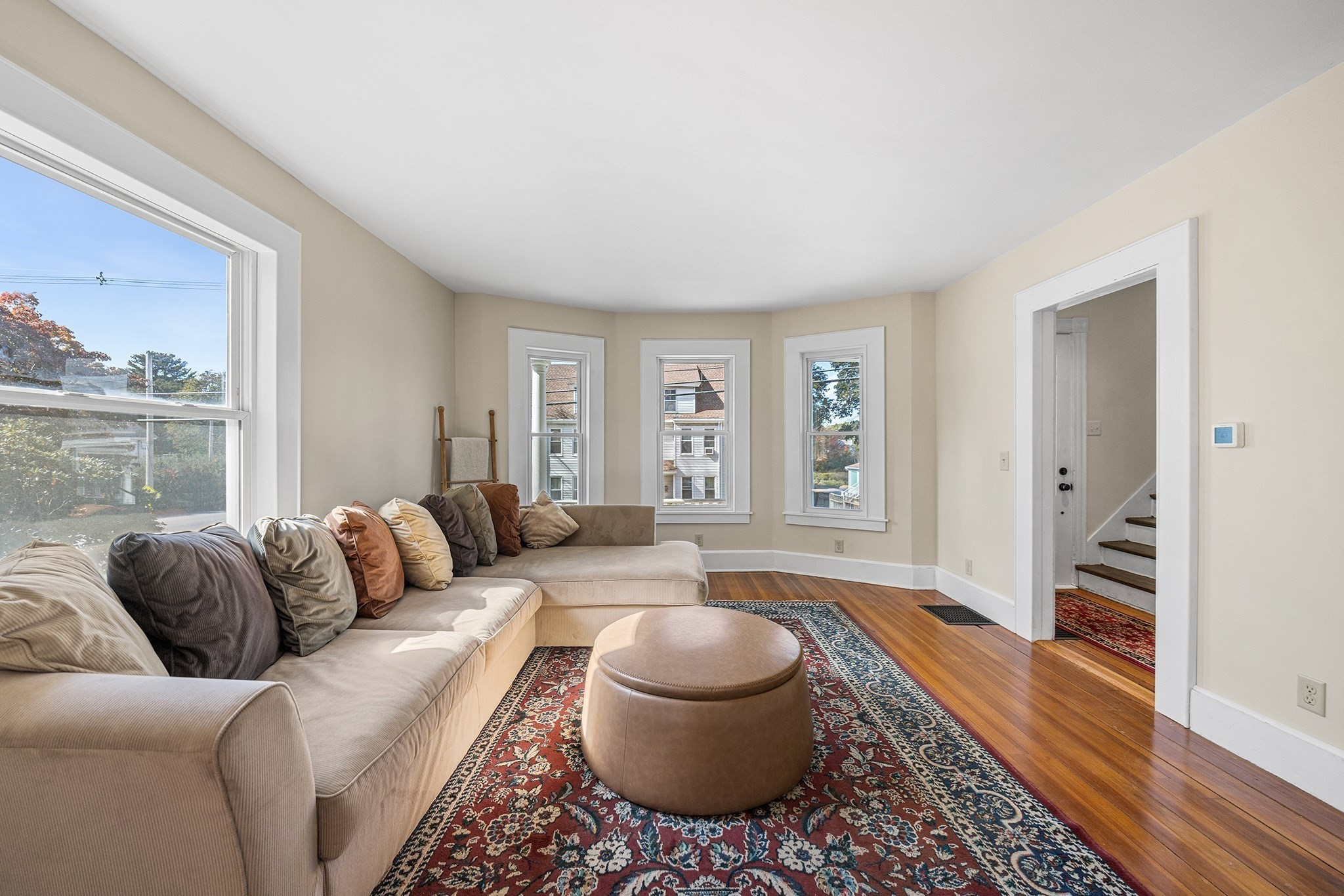 Living room with a beige sectional, patterned rug, hardwood floors, and tall windows.
