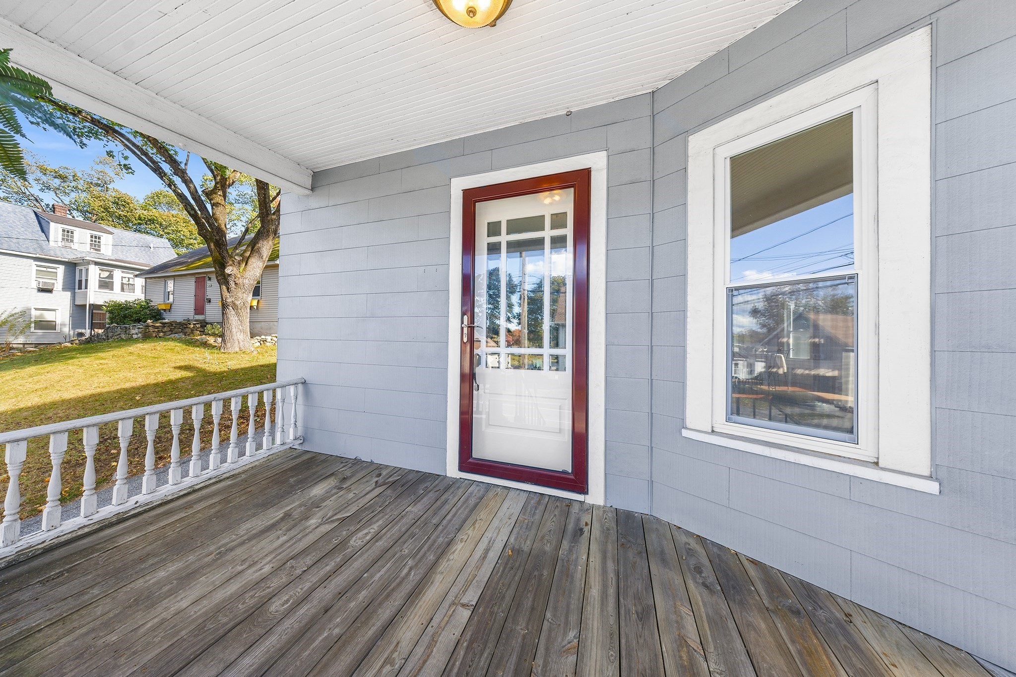 Covered porch with weathered decking, white railing, and a storm door framed in dark red trim.