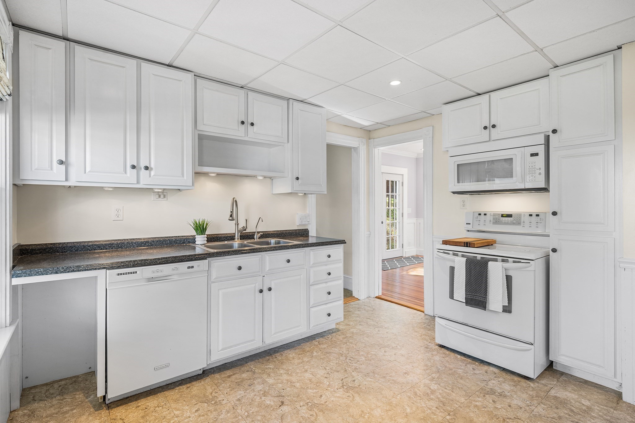 Kitchen with white cabinets, dark countertops, double sink, and white appliances.