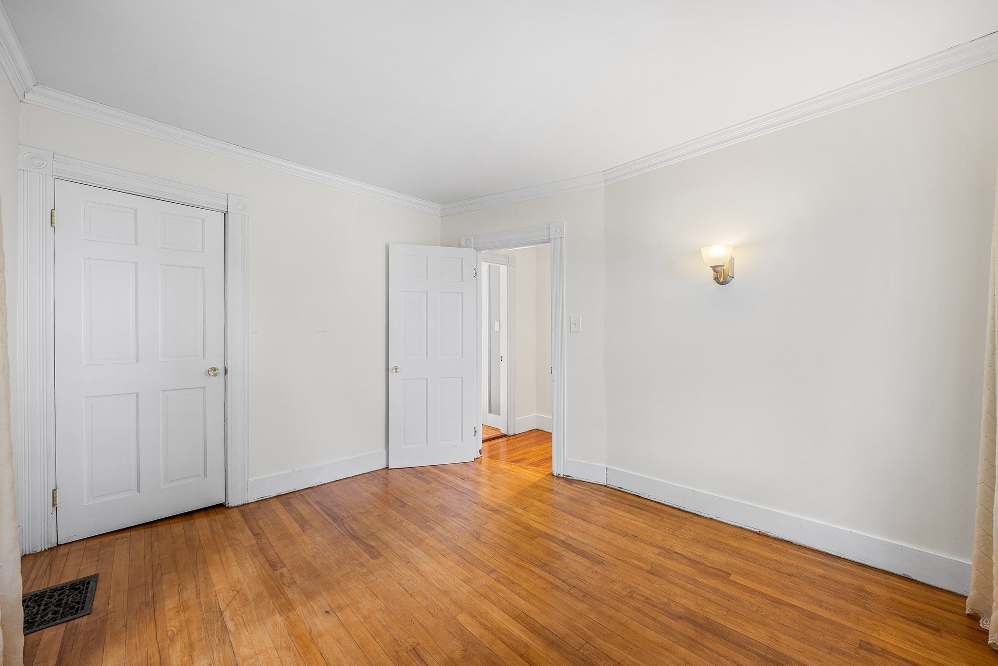 Empty room with hardwood floors, paneled doors, ornate white trim, and a wall sconce.