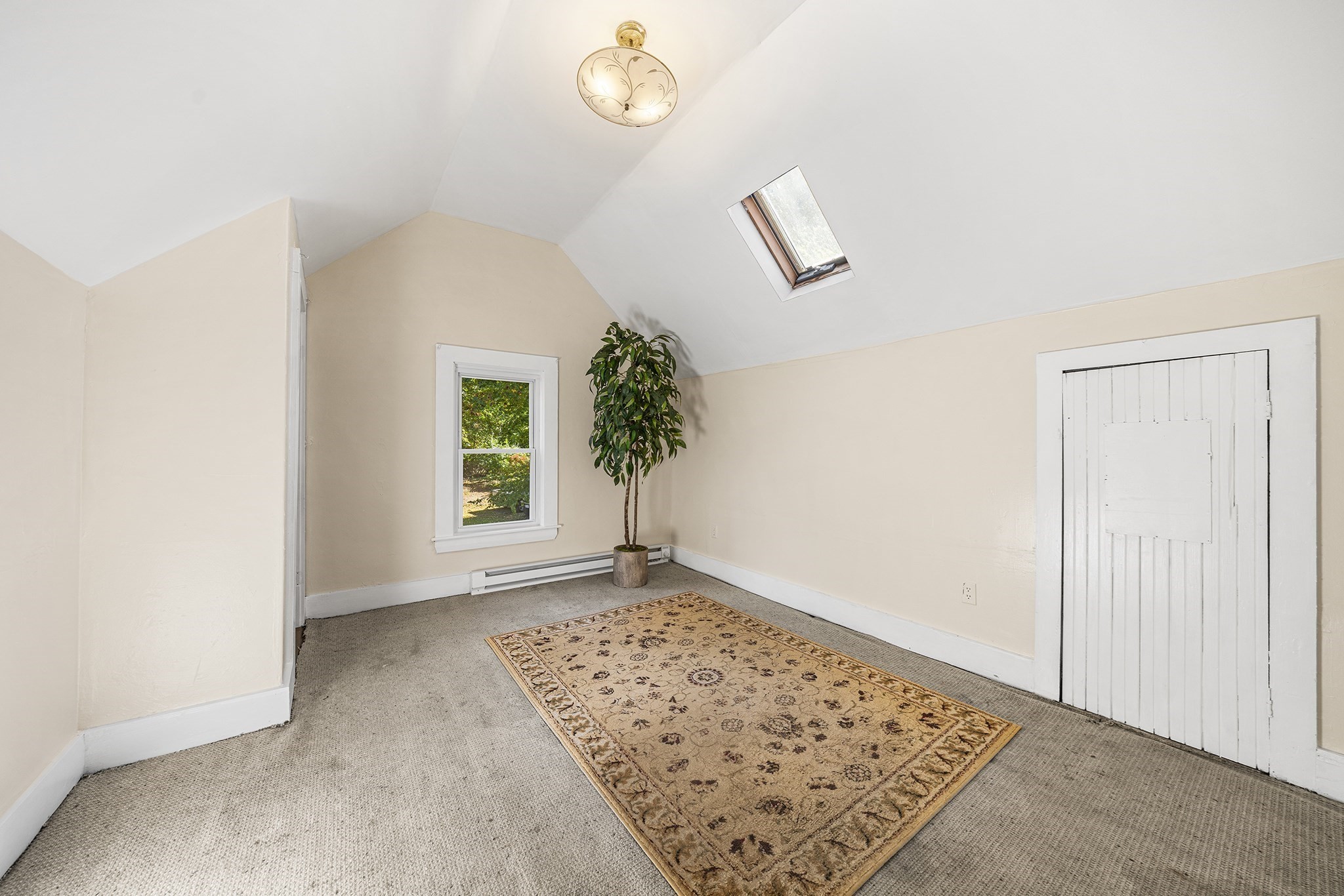Attic room with a sloped ceiling, skylight, and patterned rug on gray carpet.