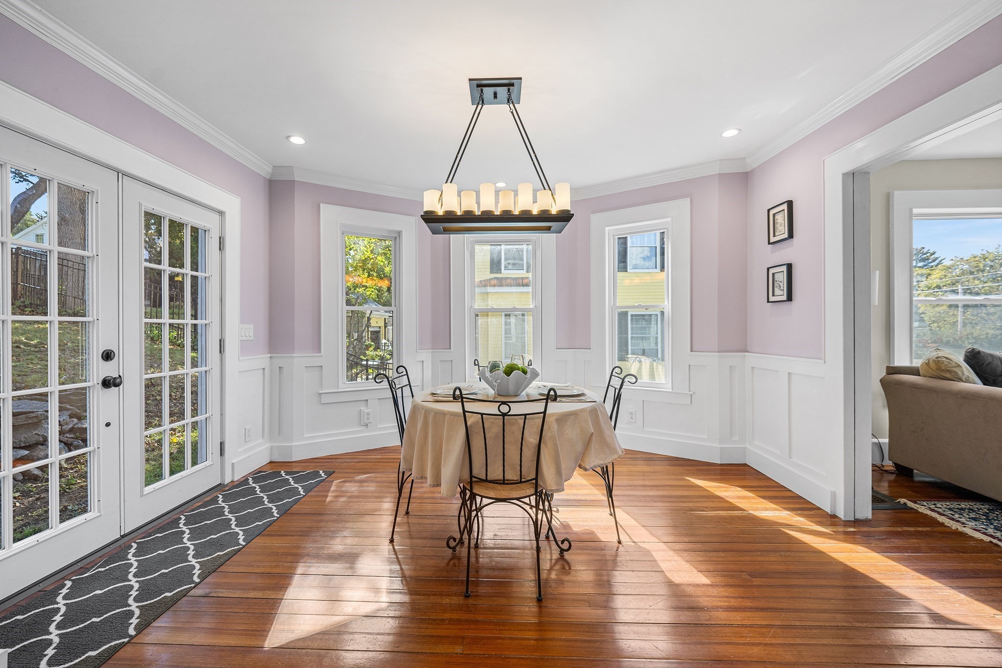 Dining room with a round table, lavender walls, white wainscoting, and polished hardwood floors.