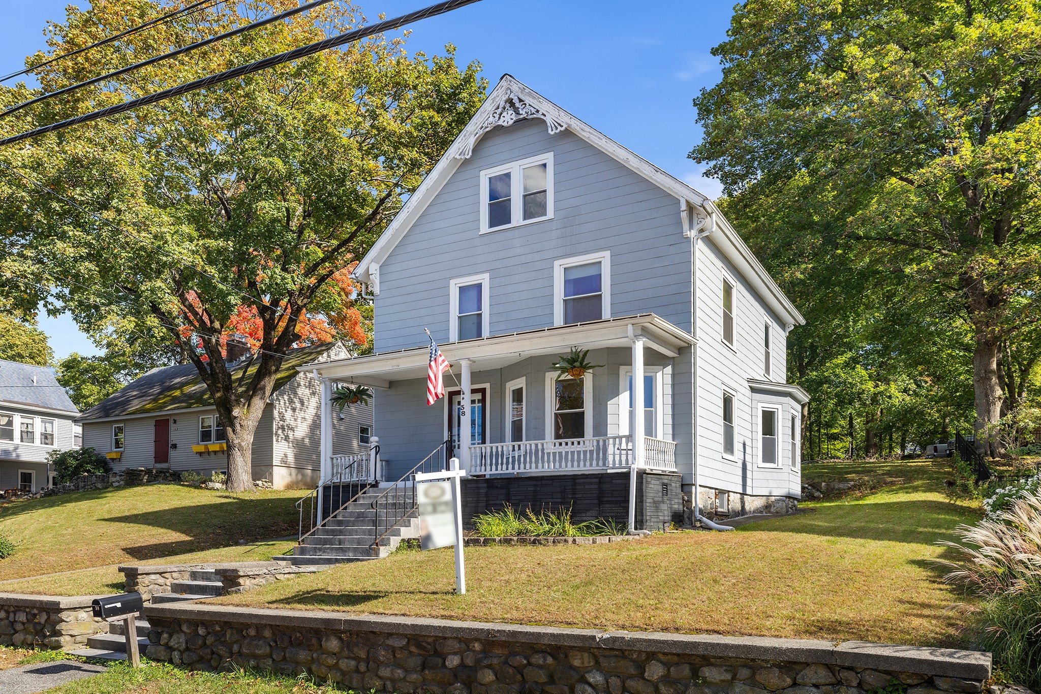 Gray two-story house with ornate gable trim, covered porch, and stone retaining walls.