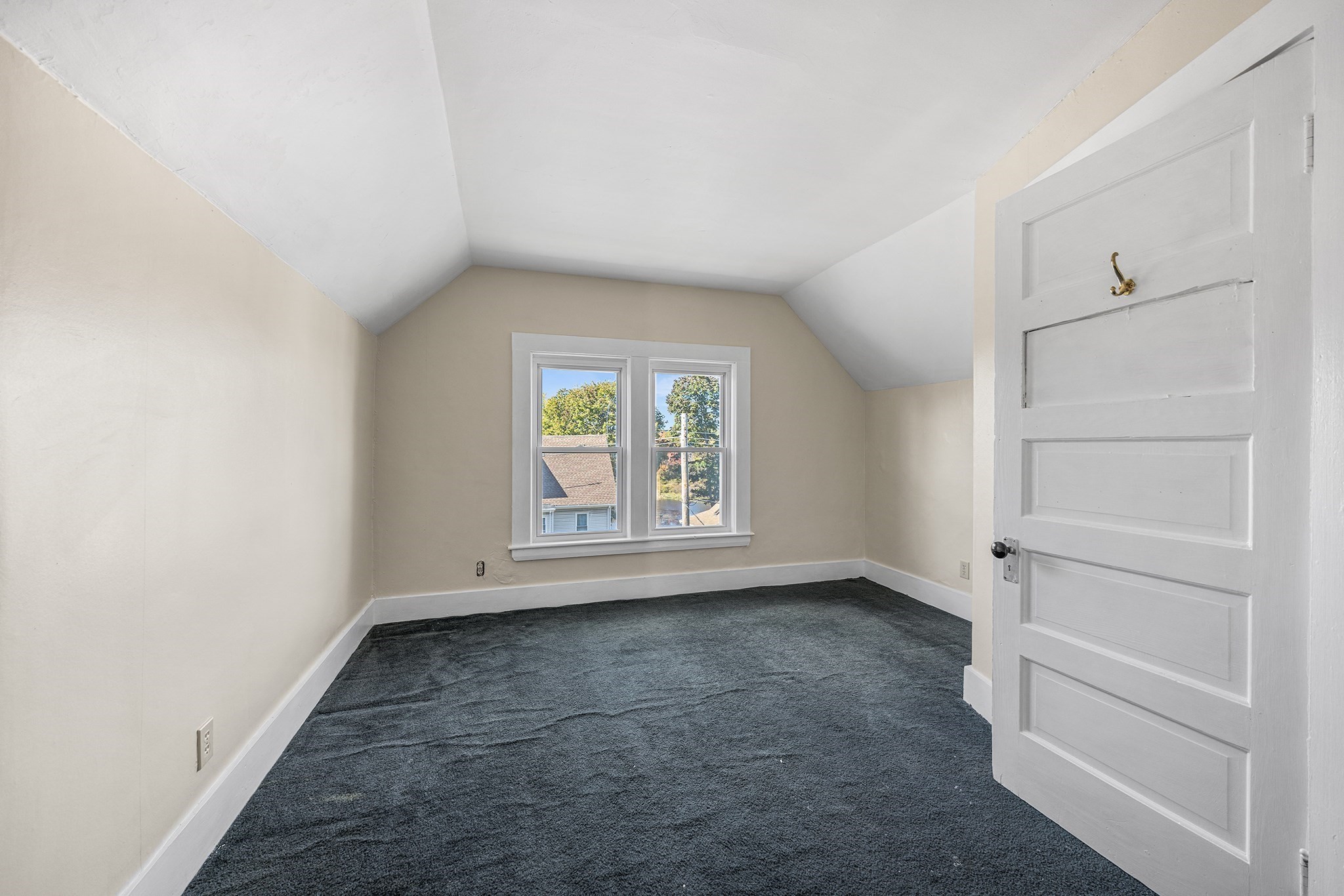 Empty upstairs room with a sloped ceiling, dark carpet, and two windows.