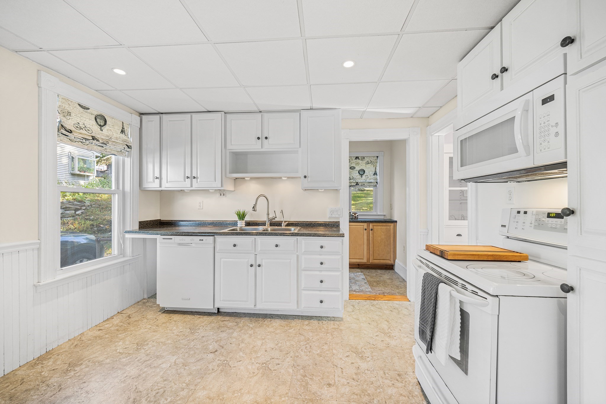 Kitchen with white cabinetry, a double-basin sink, and electric range beneath a microwave.