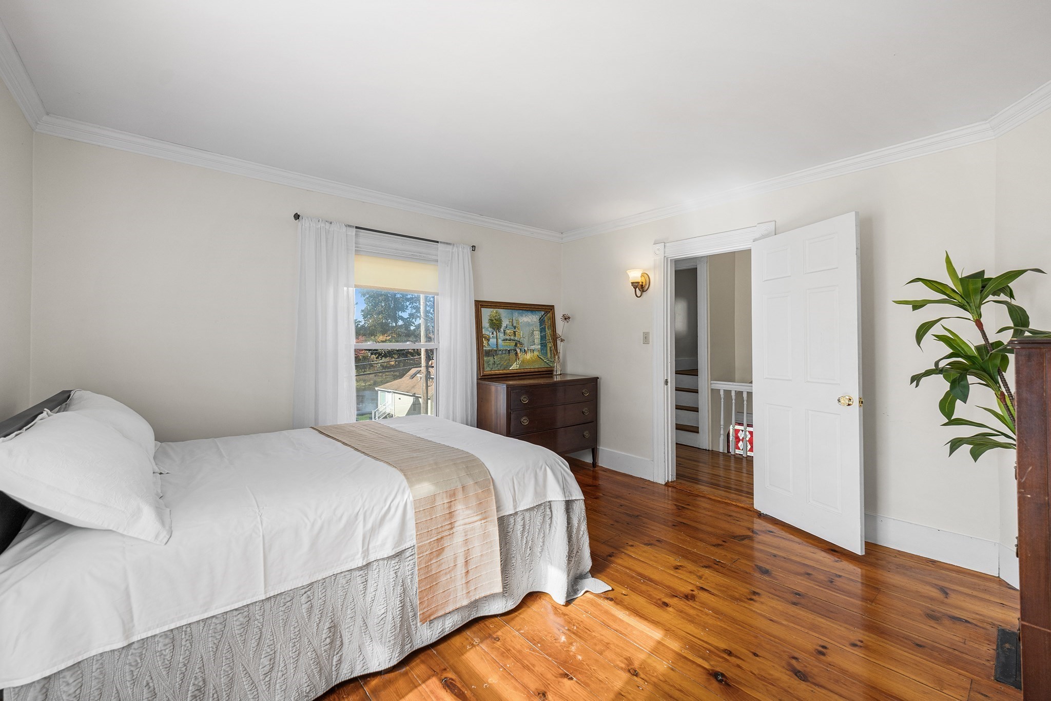 Furnished bedroom with polished hardwood floors, a white bed, and an open doorway to the stairs.
