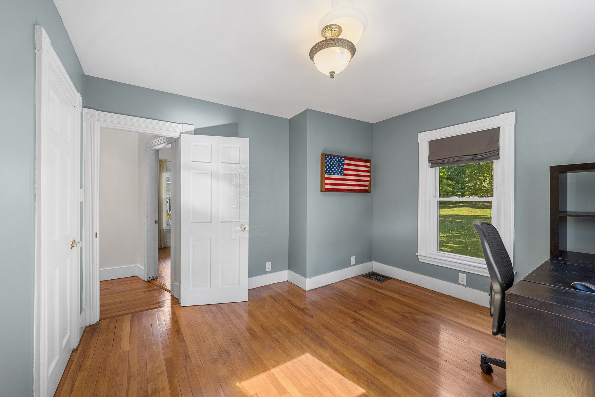 Room with blue-gray walls, hardwood floors, a window, and framed American flag.