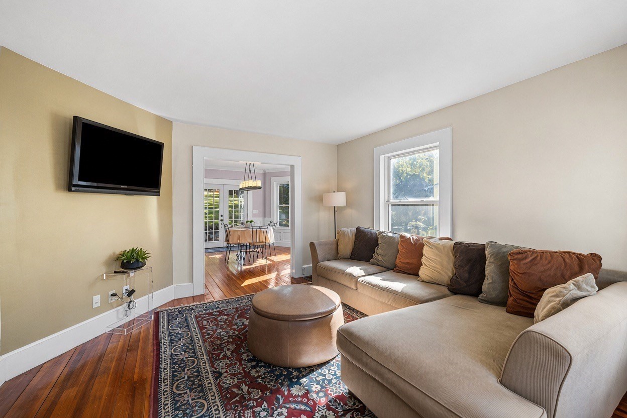 Living room with a beige sectional, patterned rug, hardwood floors, and a doorway to the dining area.