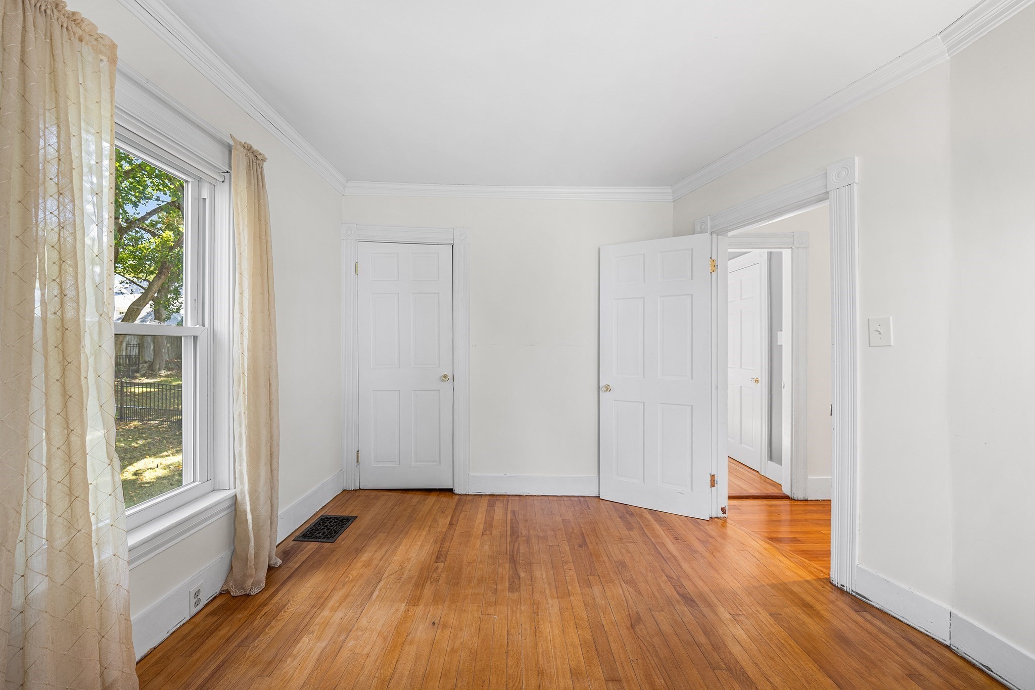 Empty room with hardwood floors, a curtained window, and open doorways.