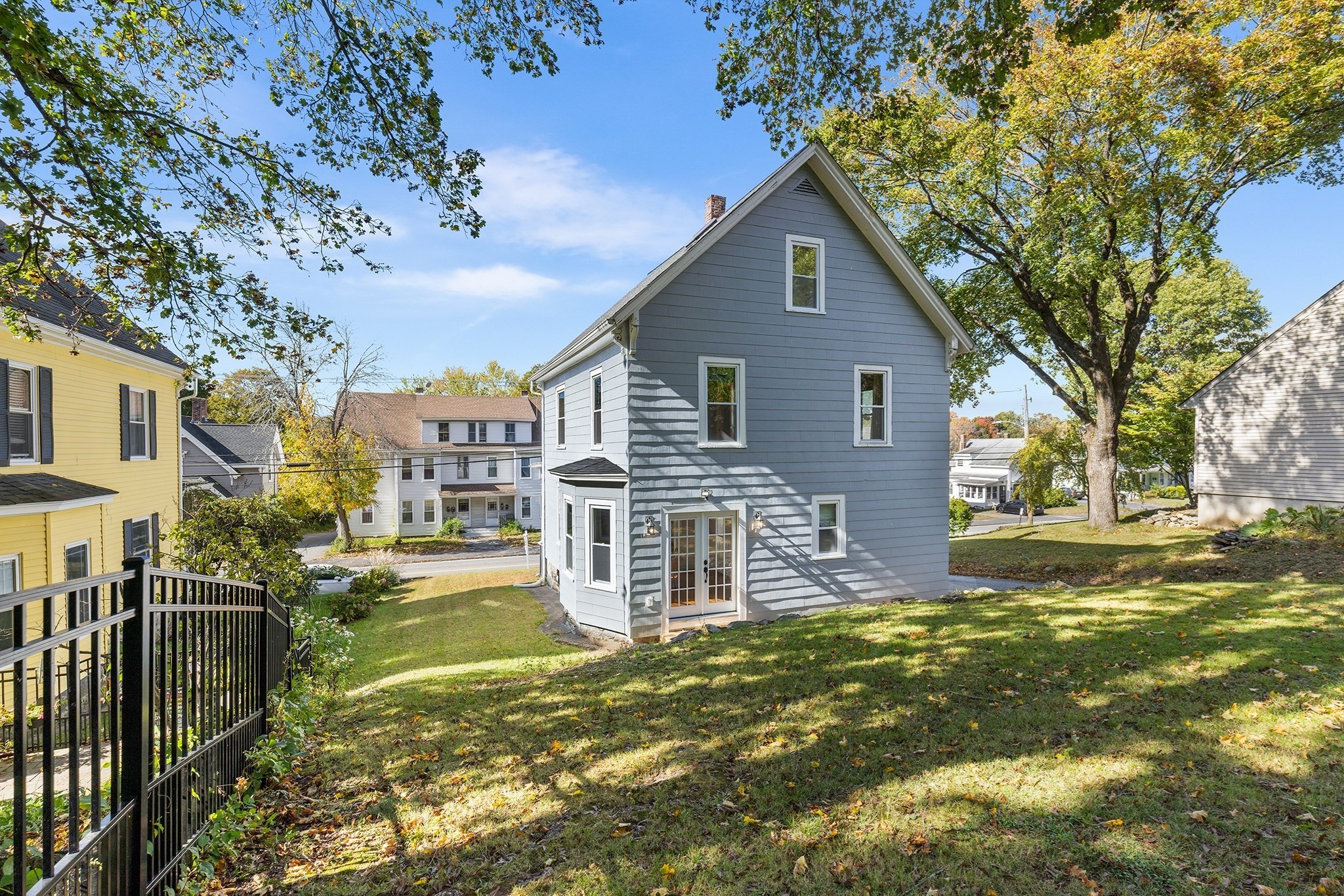 Gray gabled house with white trim and glass doors above a shaded, sloping lawn.