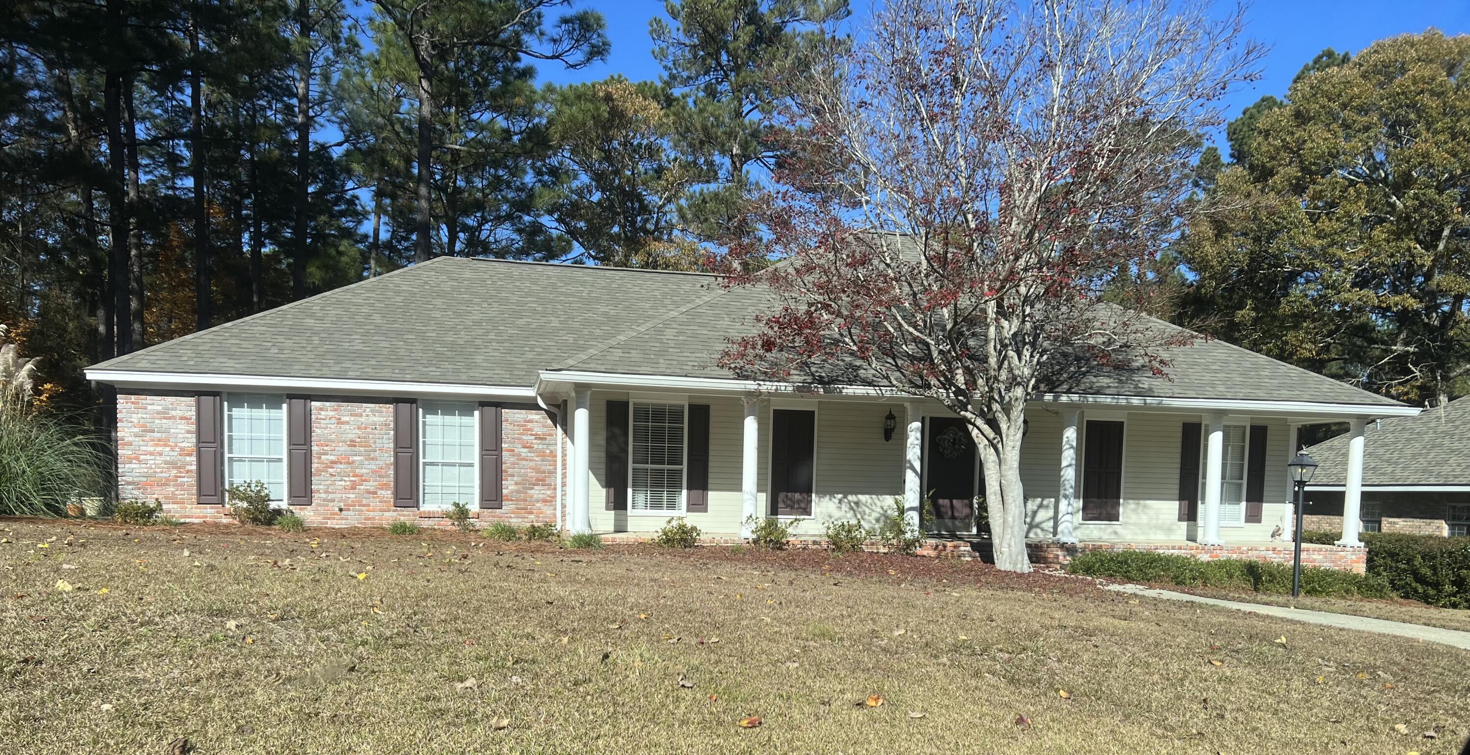 Single-story brick-and-siding home with a columned porch and a red-leaved tree in front.