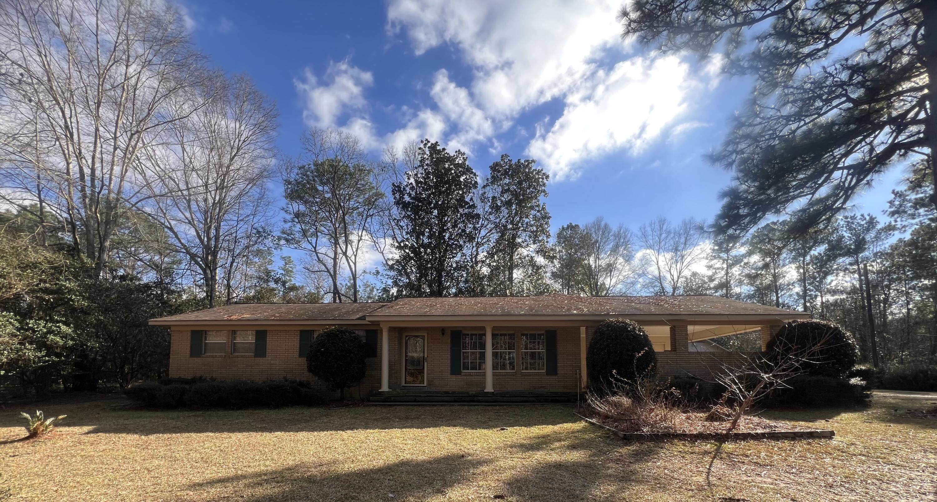 Single-story brick ranch home with a covered porch and attached carport, surrounded by mature trees.