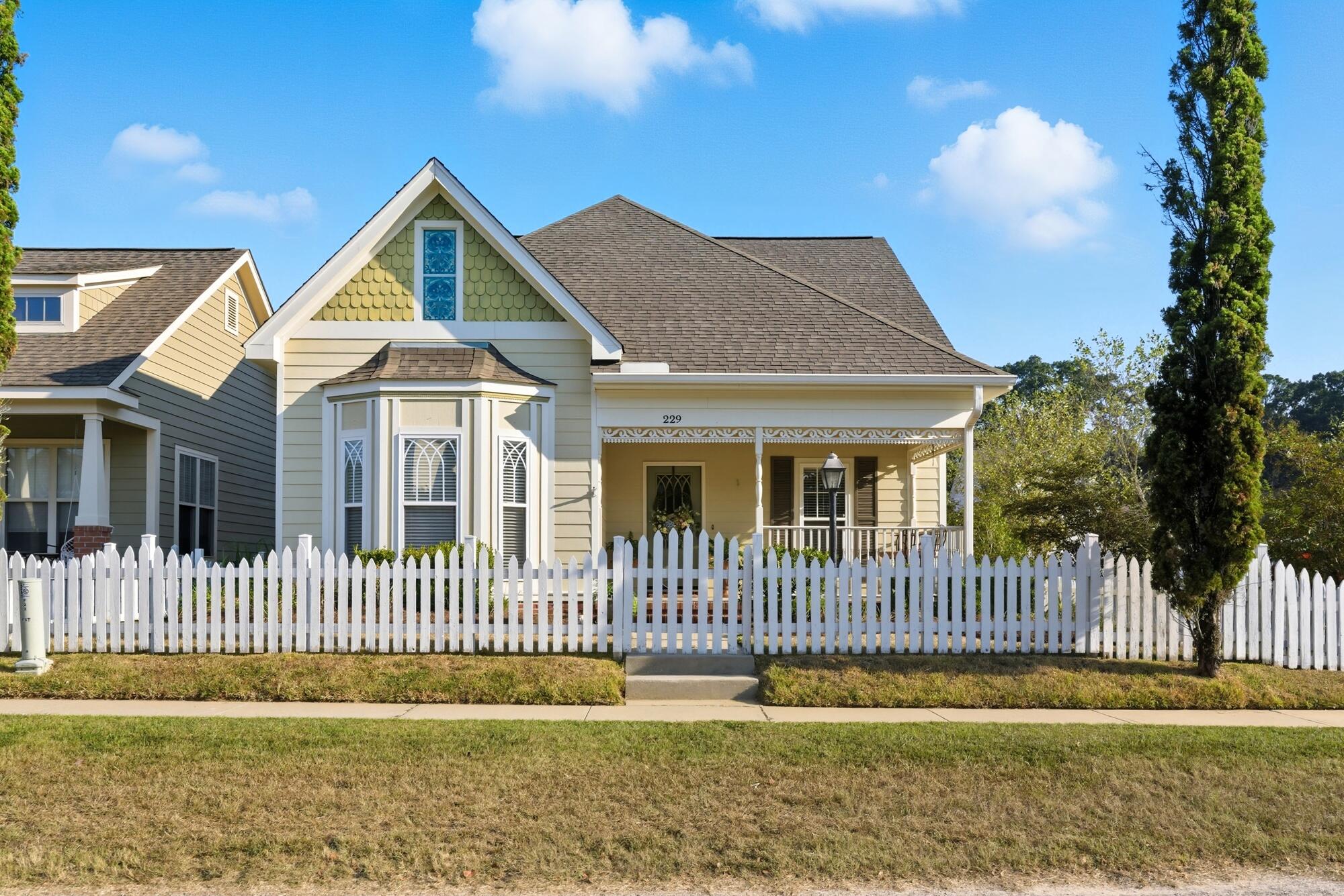 Cream house with a blue stained-glass gable window and white picket fence.