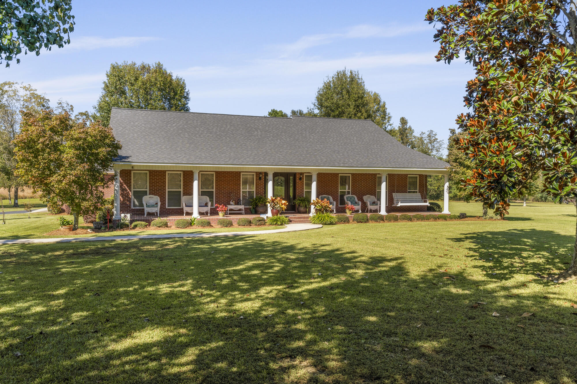 Single-story brick home with a columned front porch, porch seating, and a broad shaded lawn.
